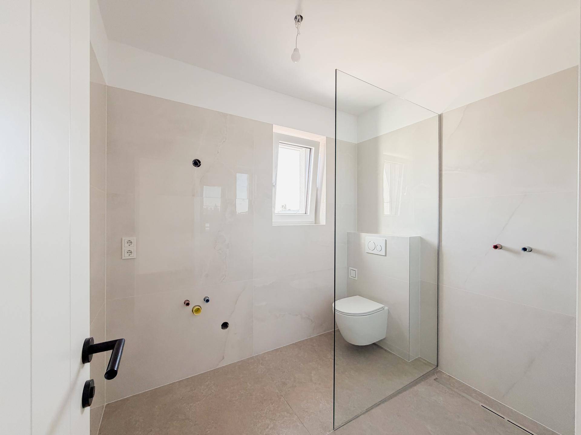 Modernes Badezimmer mit hellen Fliesen, wandhängendem WC und bodengleicher Dusche.