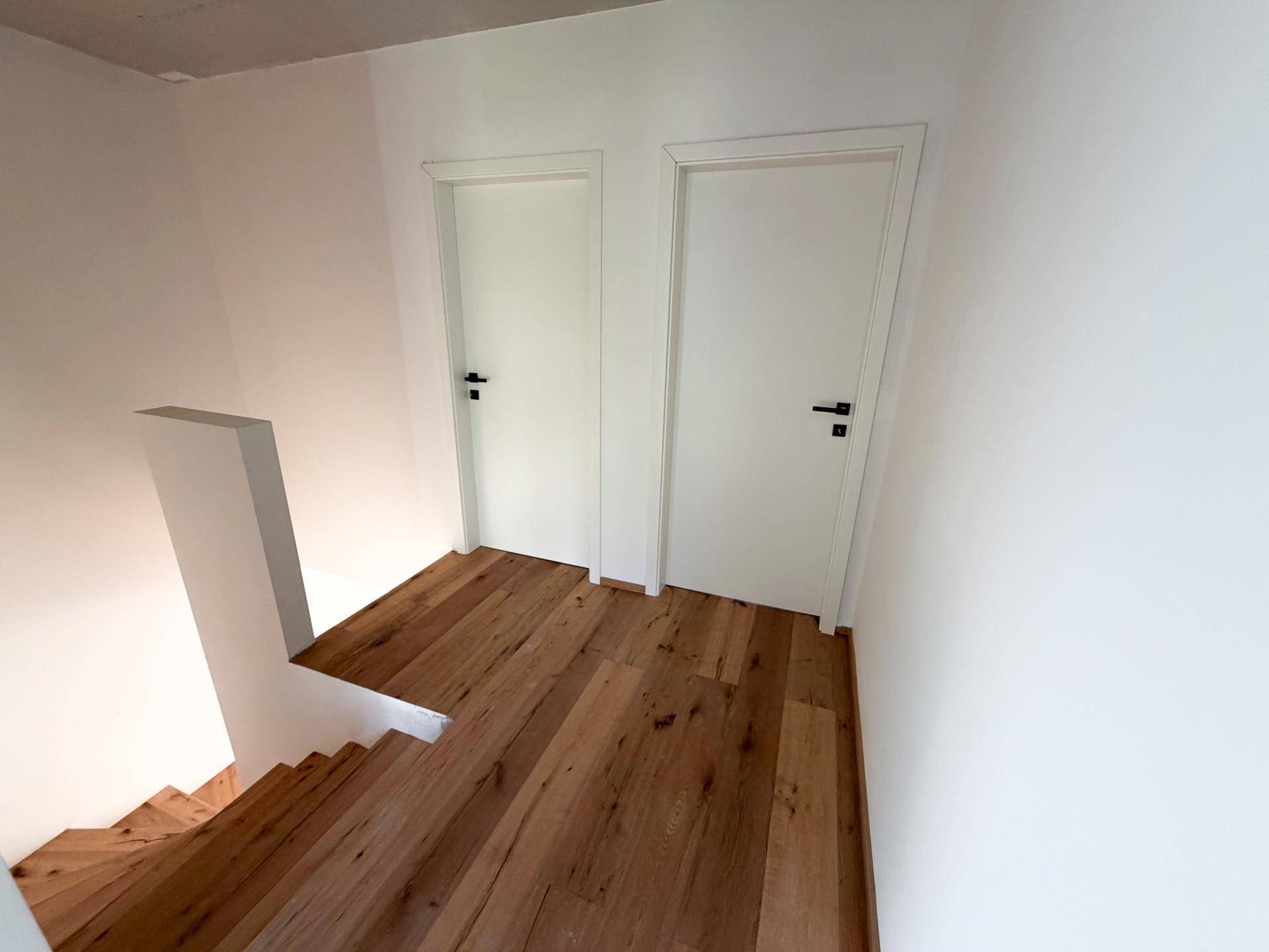 Holztreppe führt zu einem oberen Bereich mit zwei weißen Türen.