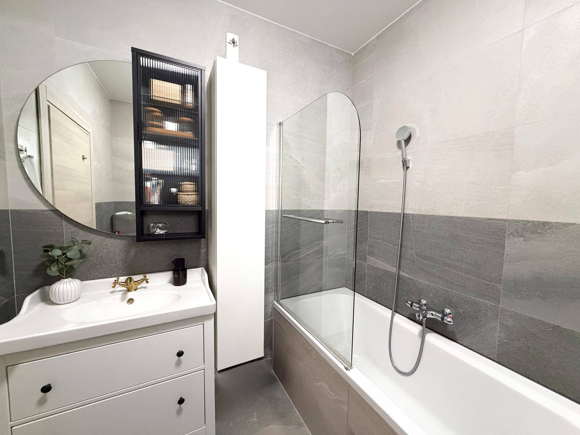 Stilvolles Badezimmer mit Badewanne, runden Spiegel und praktischem Hängeschrank.
