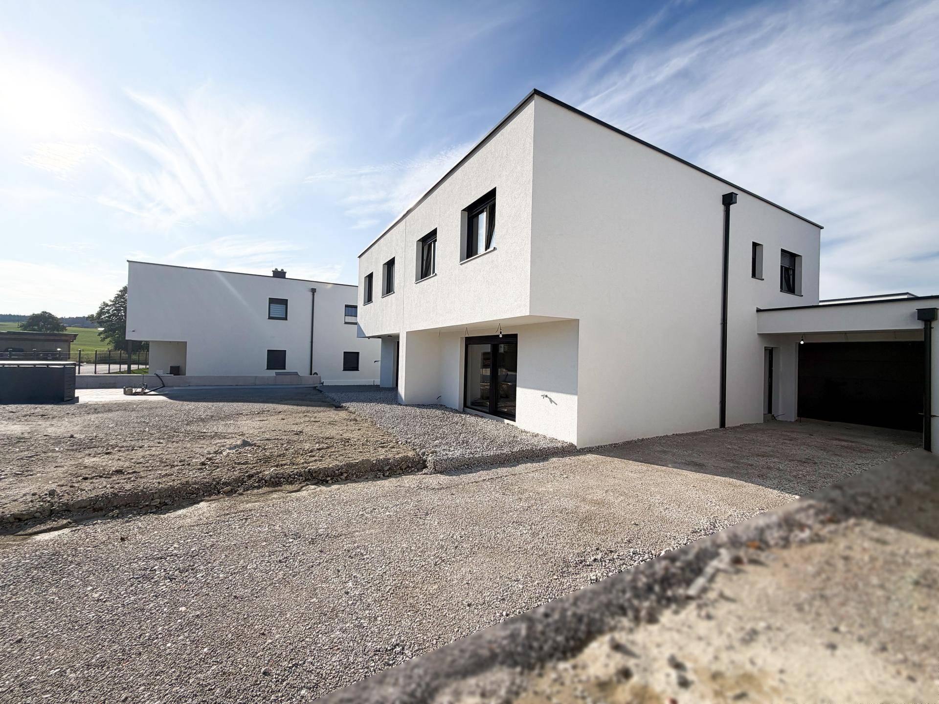 Weiß verputzte moderne Neubauten mit dunklen Fenstern und Flachdächern in ländlicher Umgebung.