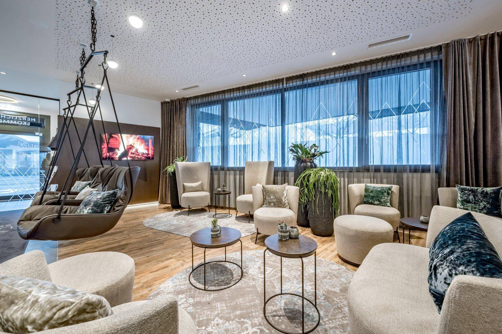 Gemütlicher Loungebereich mit modernen Möbeln, Schaukelstuhl und großen Fenstern mit Blick auf die Landschaft.