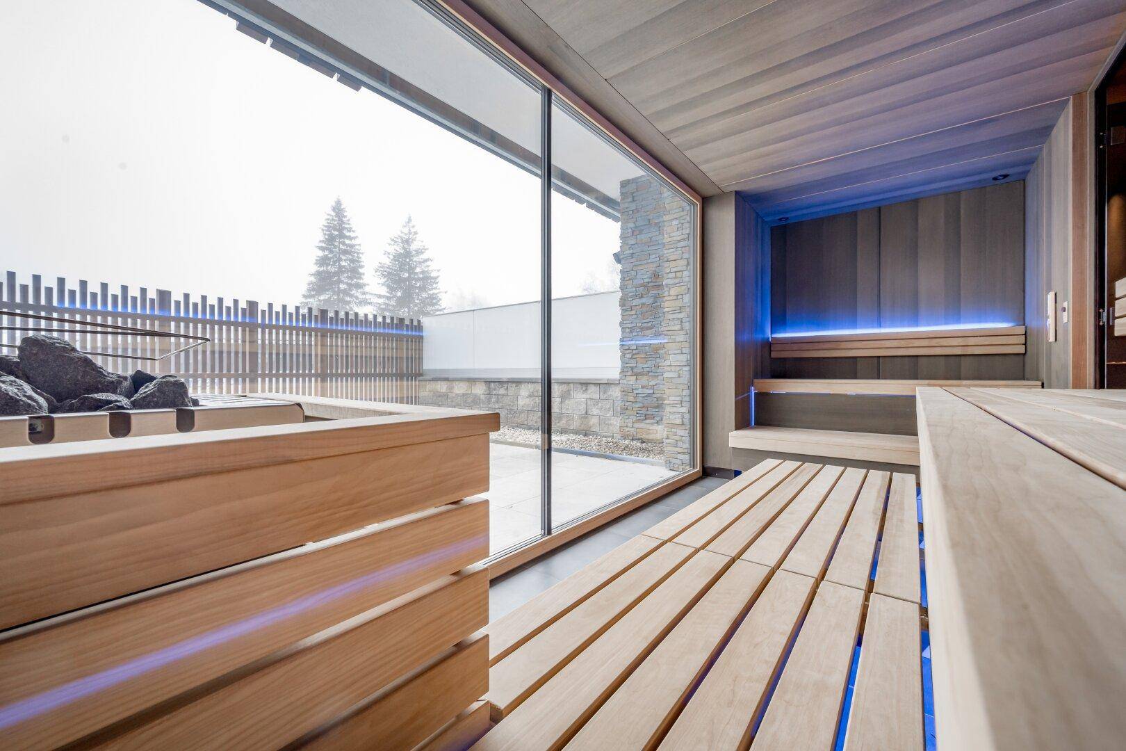 Moderne Sauna mit Holzverkleidung, großen Fenstern und stimmungsvoller blauer Beleuchtung für Entspannung.