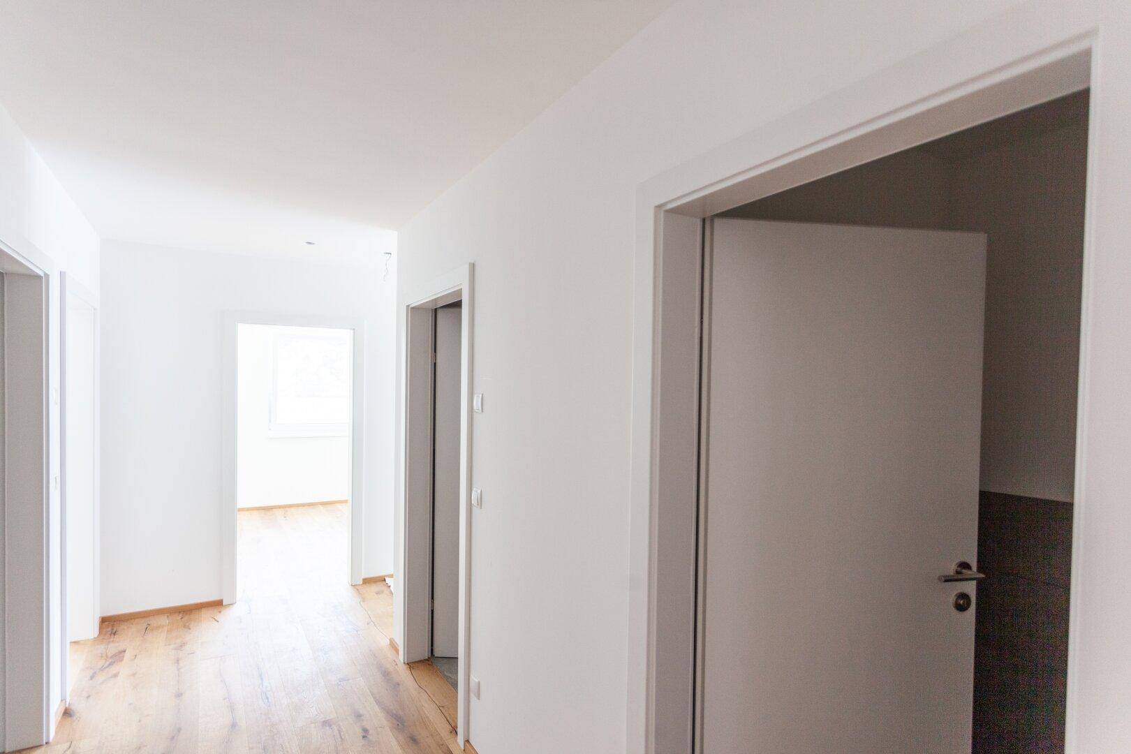 Langer, heller Flur mit mehreren Türen und Holzboden, der verschiedene Räume verbindet.