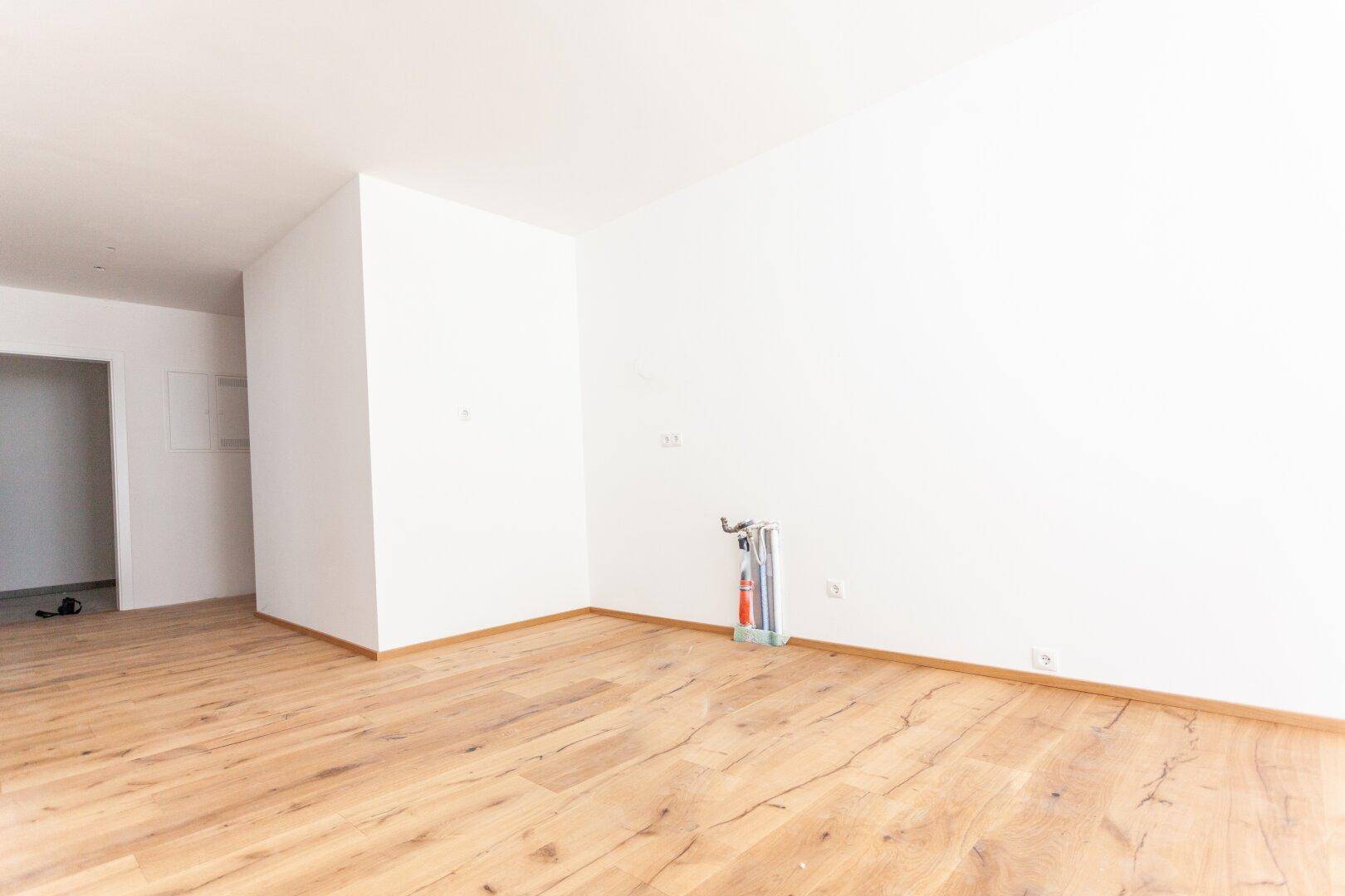 Leerer Küchenbereich mit sichtbaren Anschlüssen für eine Einbauküche und elegantem Holzfußboden.
