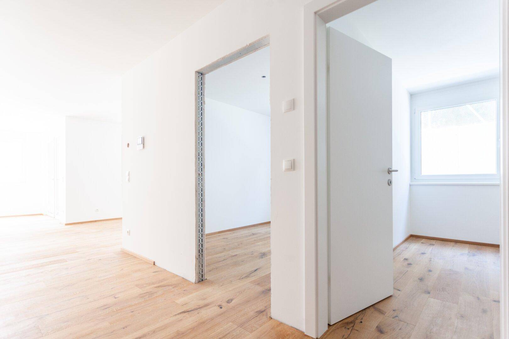 Heller Innenraum mit Holzfußboden und offener Tür zu einem weiteren Zimmer, bietet vielseitige Nutzungsmöglichkeiten.