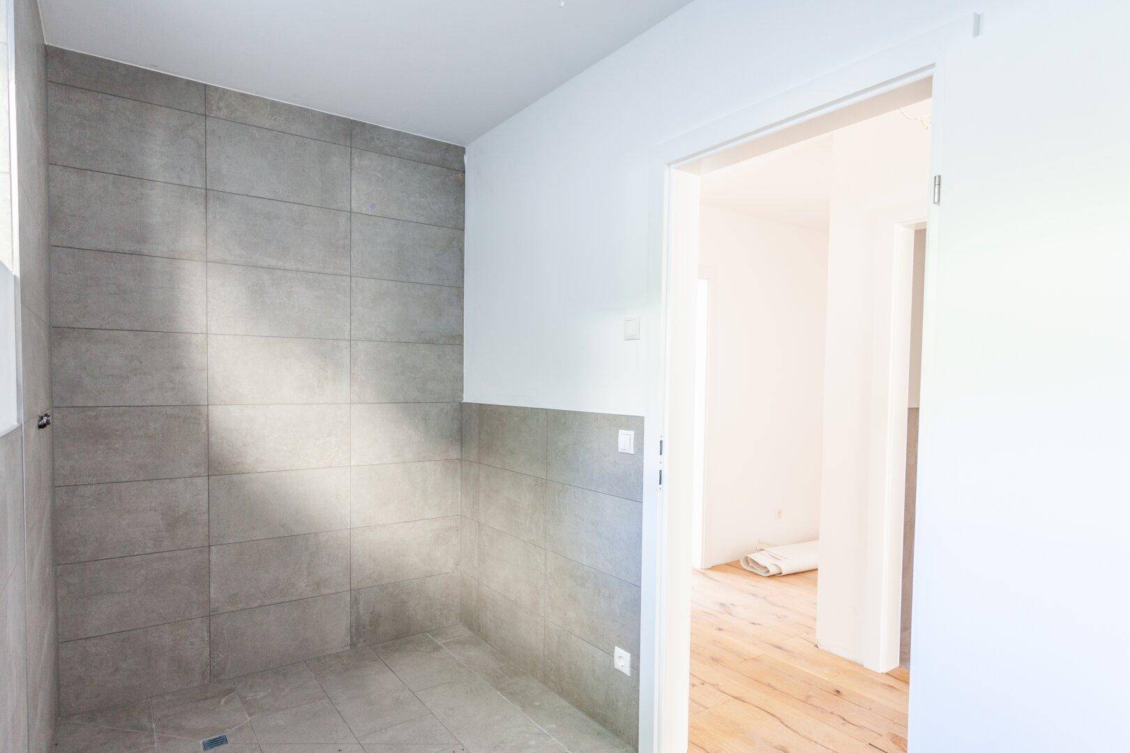 Modernes Badezimmer im Bau mit grauen Fliesen und vorbereiteter Duschfläche.