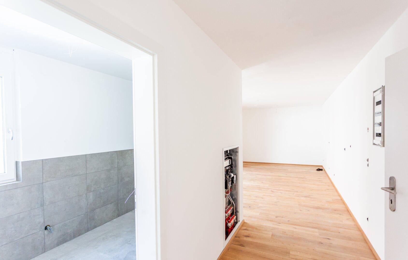 Heller Flur mit Holzboden und Blick in ein Badezimmer im Rohbauzustand, bereit für den Ausbau.