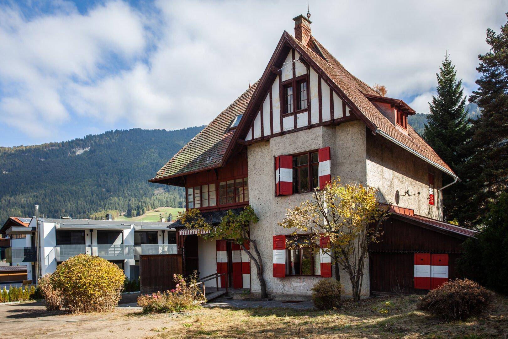 Charmantes altes Gebäude mit traditioneller Architektur, roten Fensterläden und Bergblick im Herbst.