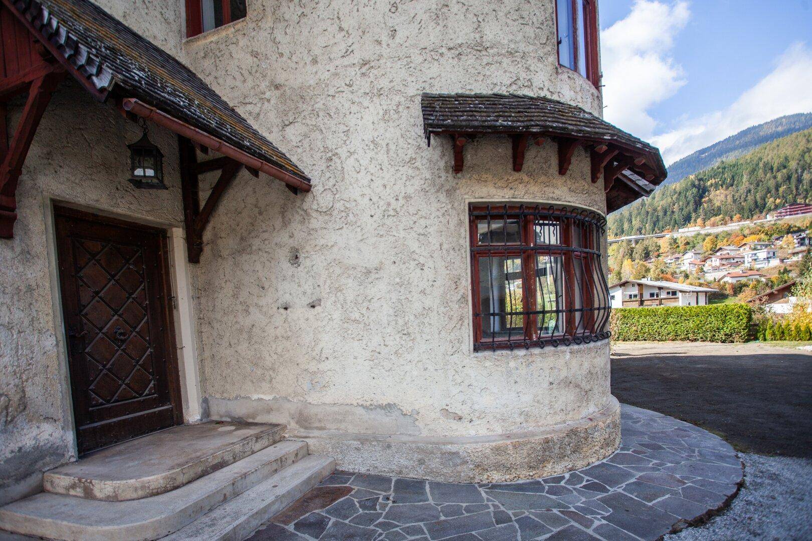 Detailansicht des Hauseingangs mit Holztür und Rundbogenfenster, umgeben von rustikalen Steinplatten.