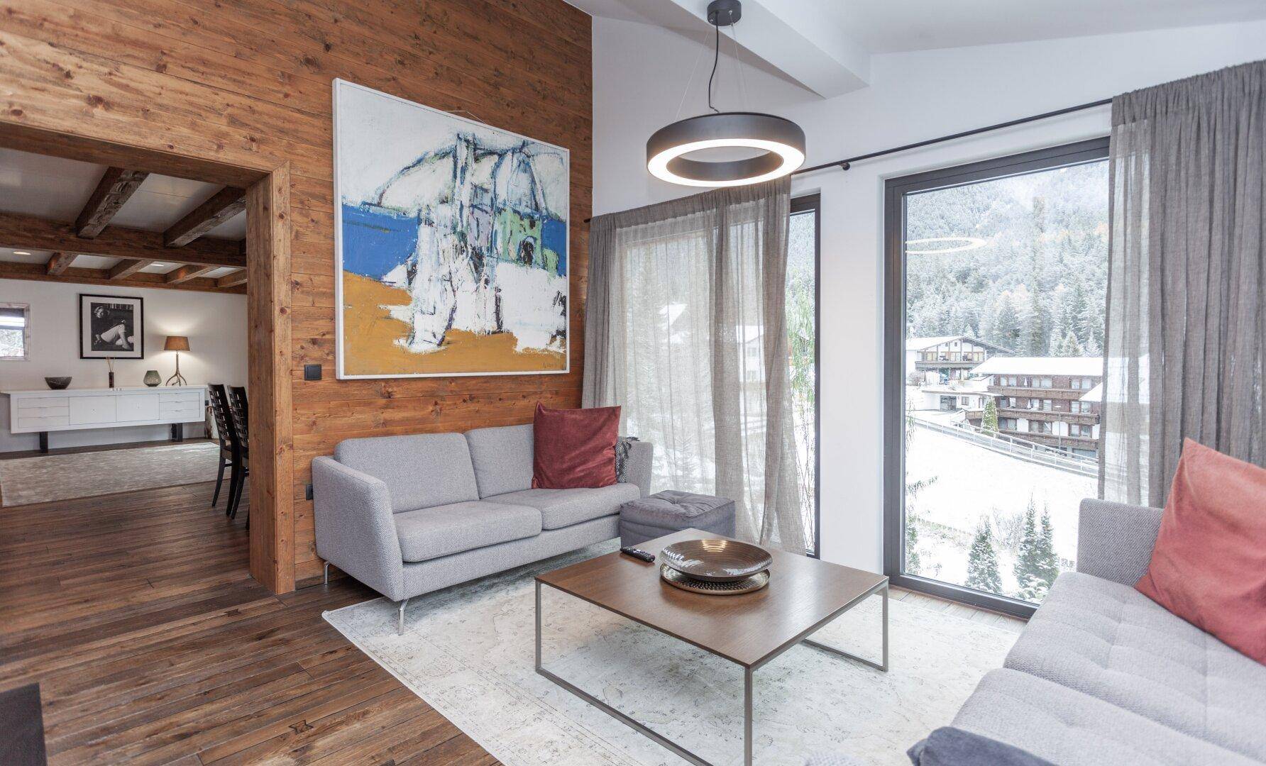 Heller Wohnbereich mit bequemen Sofas, Holzwänden und großem Fenster mit Bergblick.
