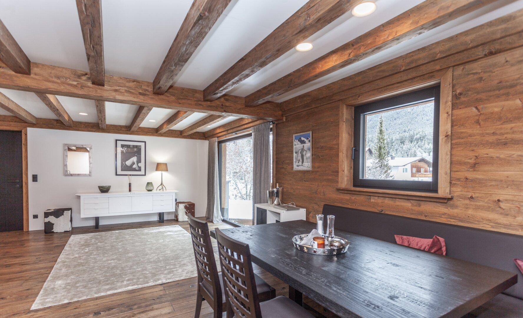 Essbereich mit Holztisch, Holzwänden und Blick auf die verschneite Umgebung durch das Fenster.