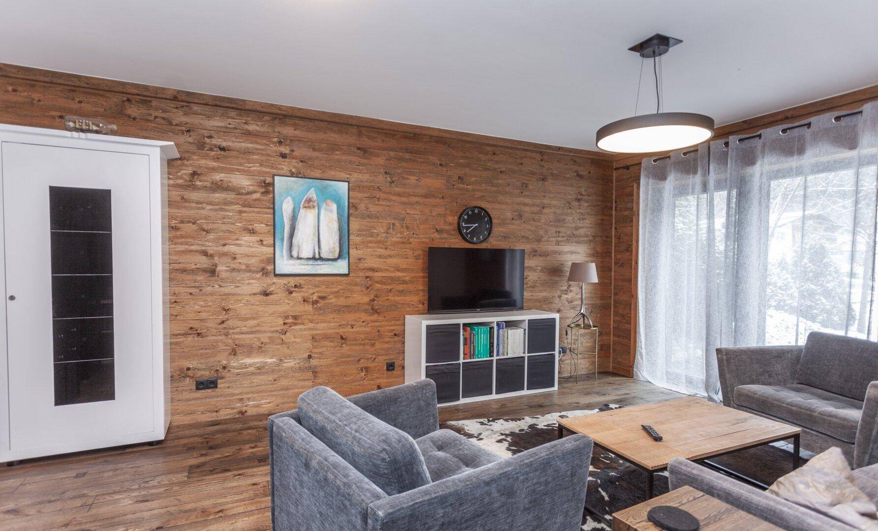 Gemütlicher Wohnbereich mit Holzwänden, bequemen Sofas und Blick auf die verschneite Landschaft.