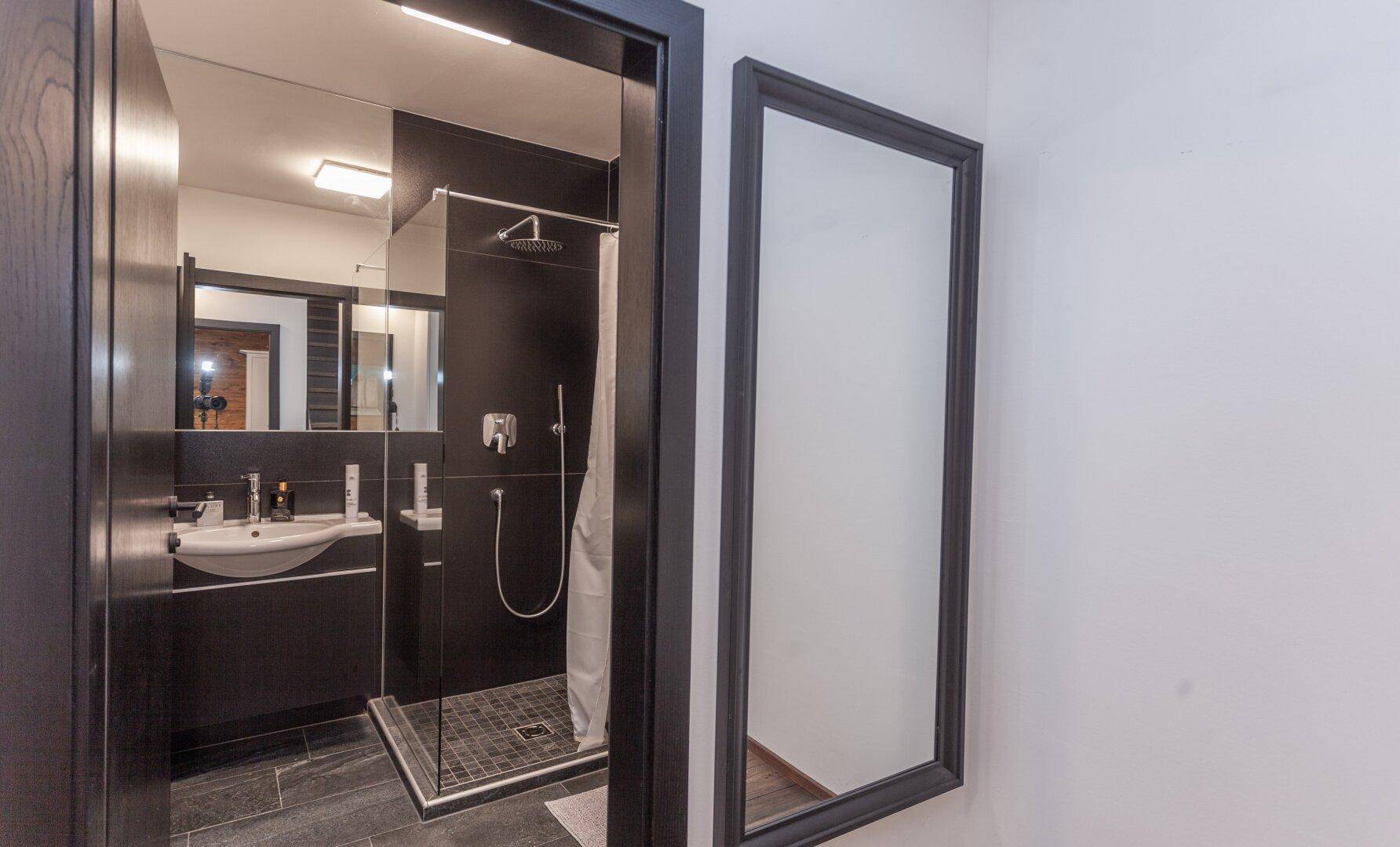 Modernes Badezimmer mit begehbarer Dusche, dunklen Fliesen und minimalistischem Design.