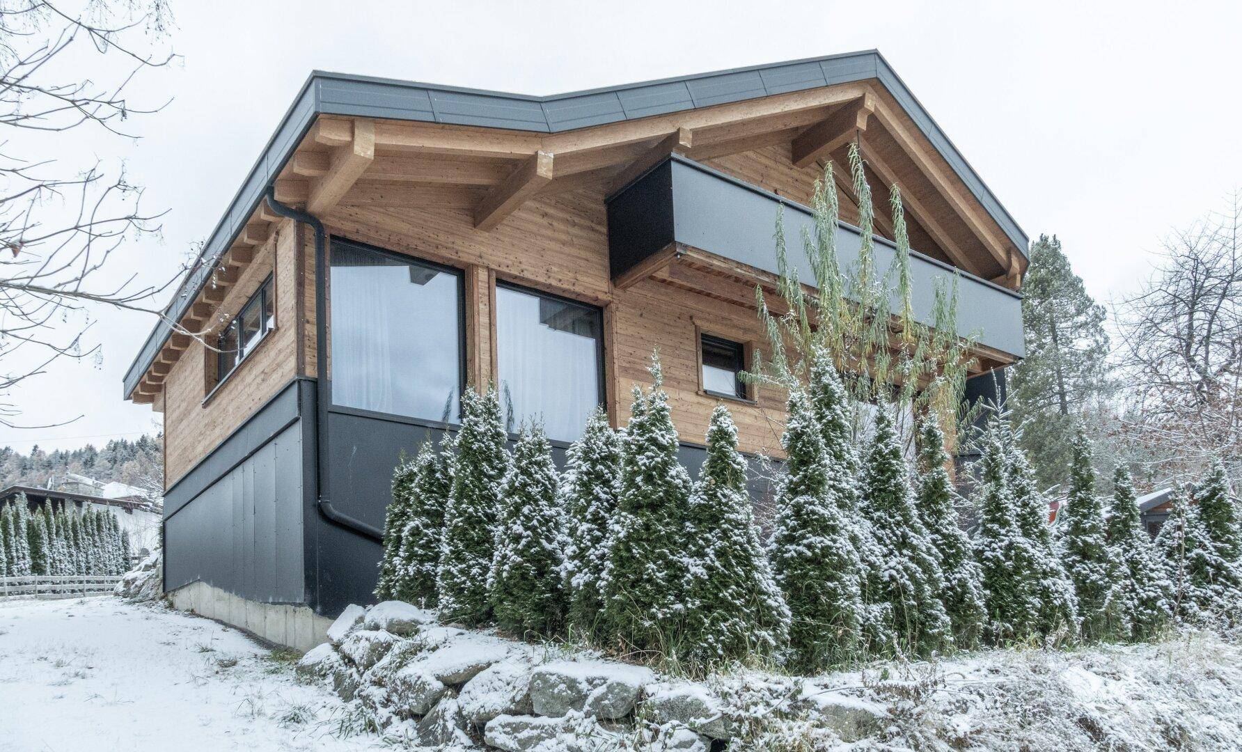 Attraktives Holzhaus mit moderner Architektur, großen Fenstern und verschneiter Landschaft.