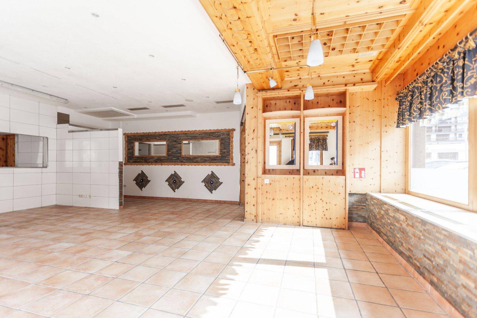 Heller Innenraum mit Holzverkleidung an Decke und Wänden, Fliesenboden und großen Fenstern.