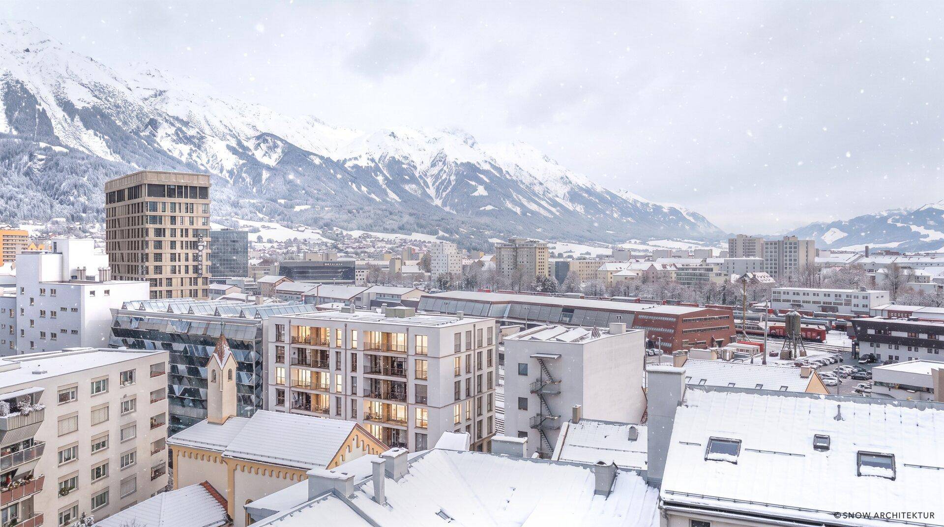 Panoramablick auf eine verschneite Stadt mit modernen Gebäuden und majestätischen Bergen im Hintergrund.