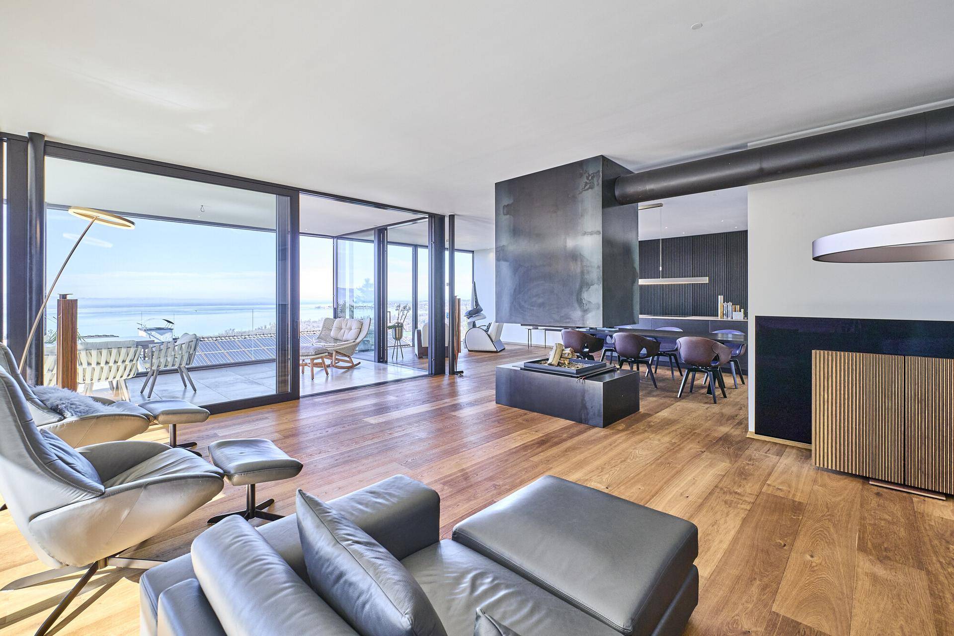 Offener Wohn- und Essbereich mit Holzboden, Kamin und Zugang zur Terrasse mit Seeblick.