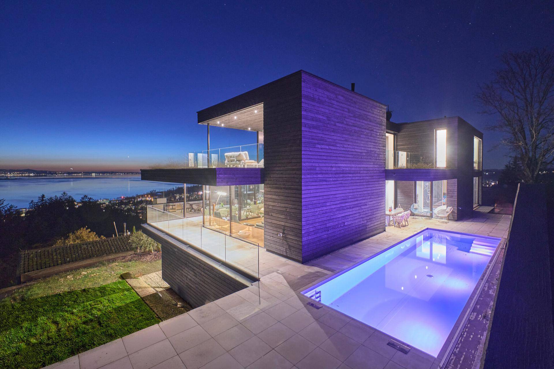 Exklusive Villa bei Nacht mit beleuchtetem Pool und atemberaubendem Blick auf den See.