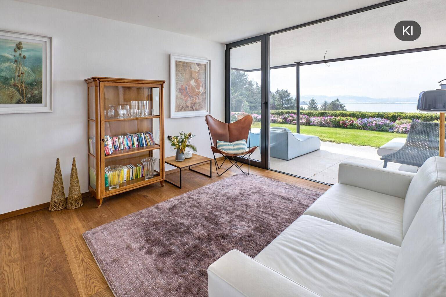 Gemütliches Wohnzimmer mit Holzboden, Bücherregal und Zugang zu einer Außenterrasse mit Seeblick.