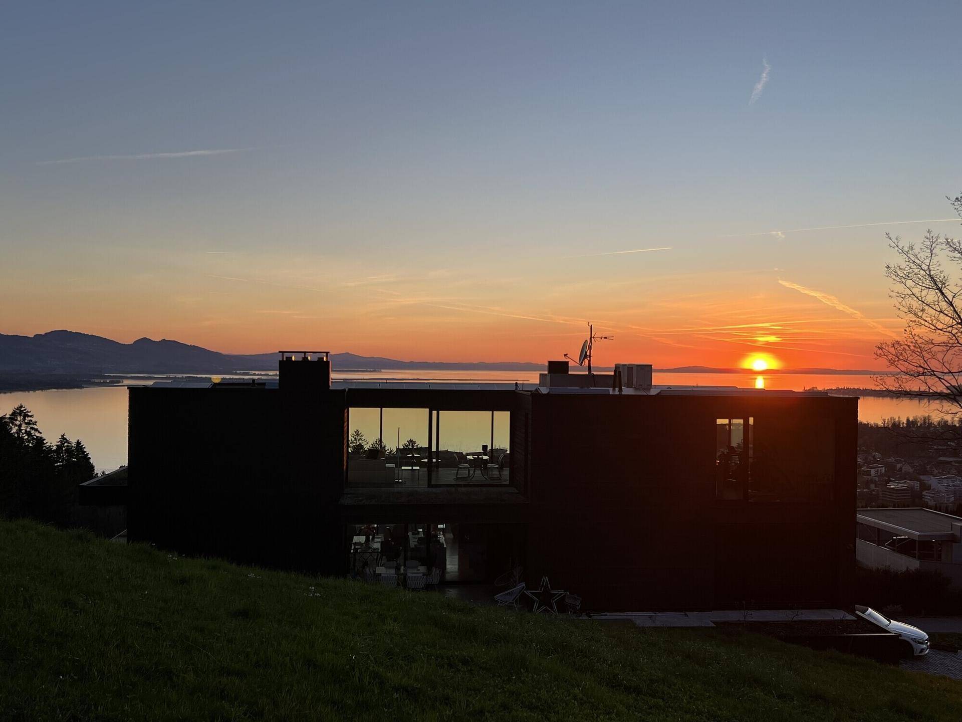 Moderne Villa bei Sonnenuntergang mit reflektierenden Fenstern und malerischem Seeblick.
