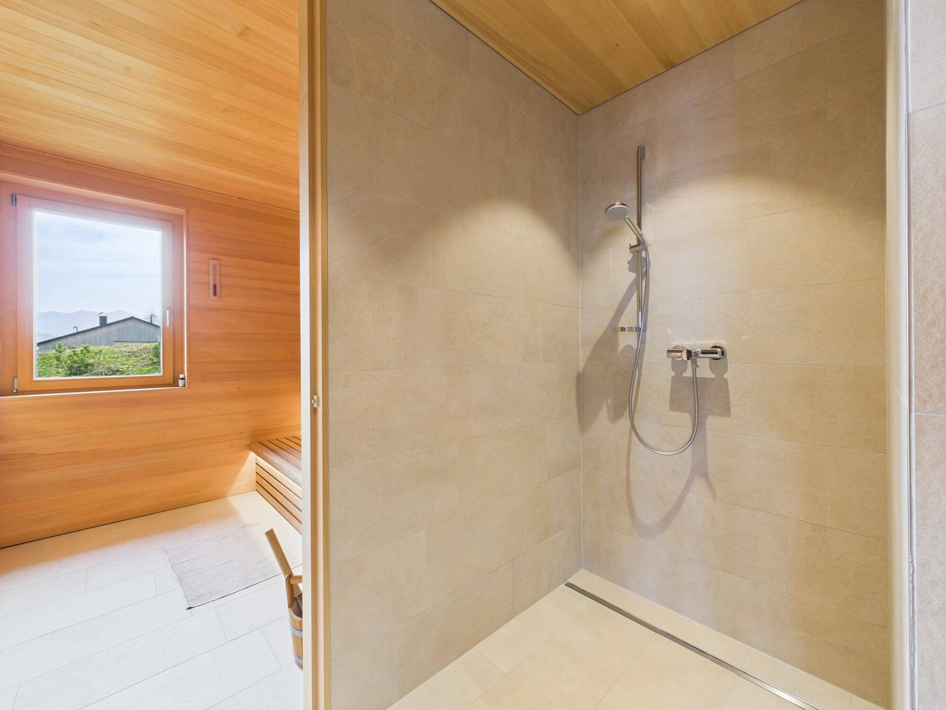 Duschbereich mit Fliesen und Zugang zu einer holzverkleideten Sauna mit Fenster.
