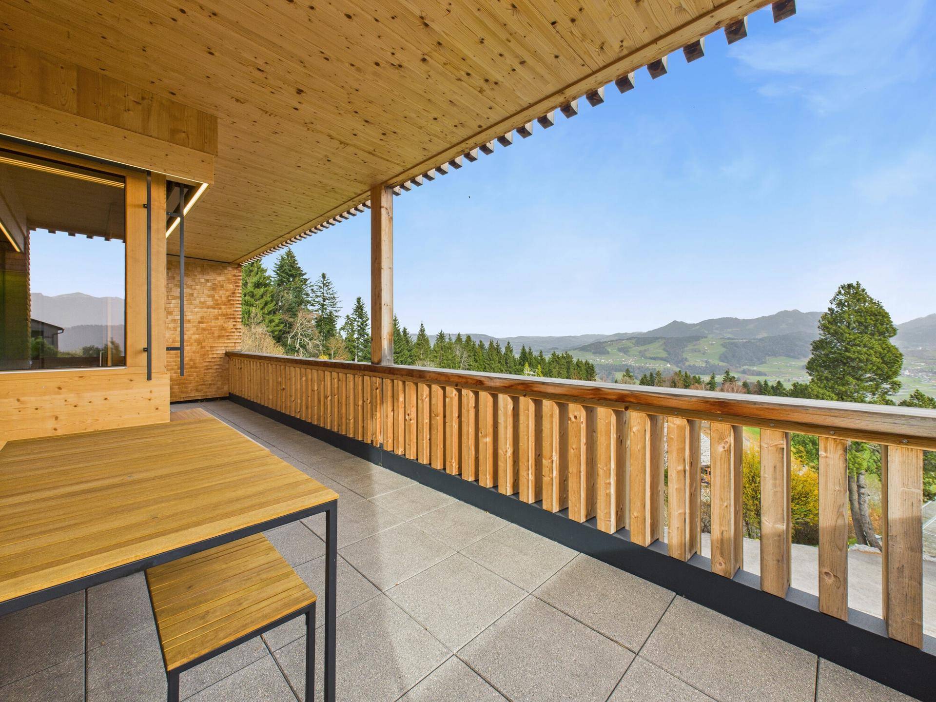 Große Terrasse mit Holzboden und -geländer, Fliesenboden und weitem Blick auf die Berge.