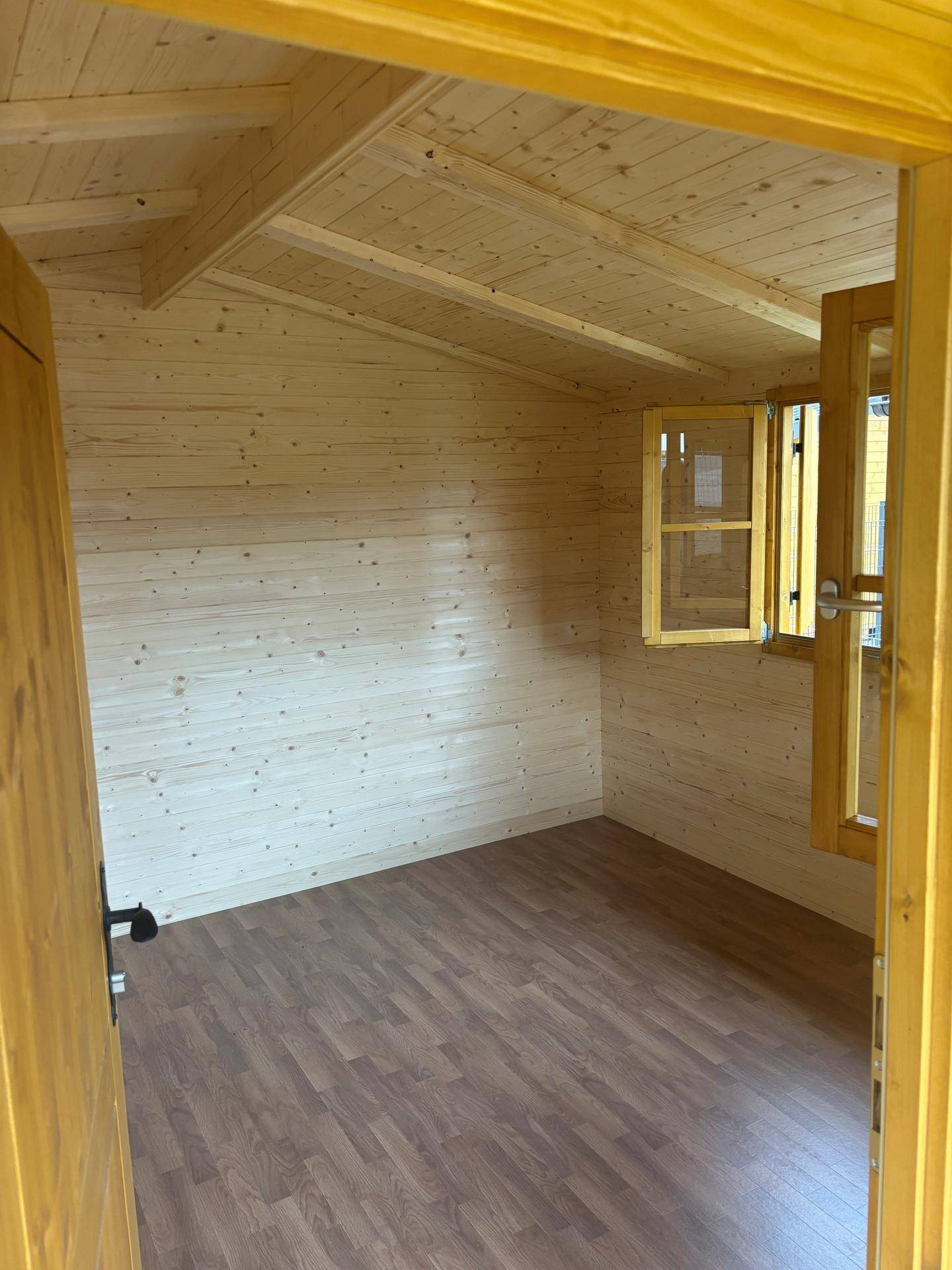 Leerer Innenraum eines Holzhauses mit Holzwänden, Holzbalkendecke und Laminatboden.