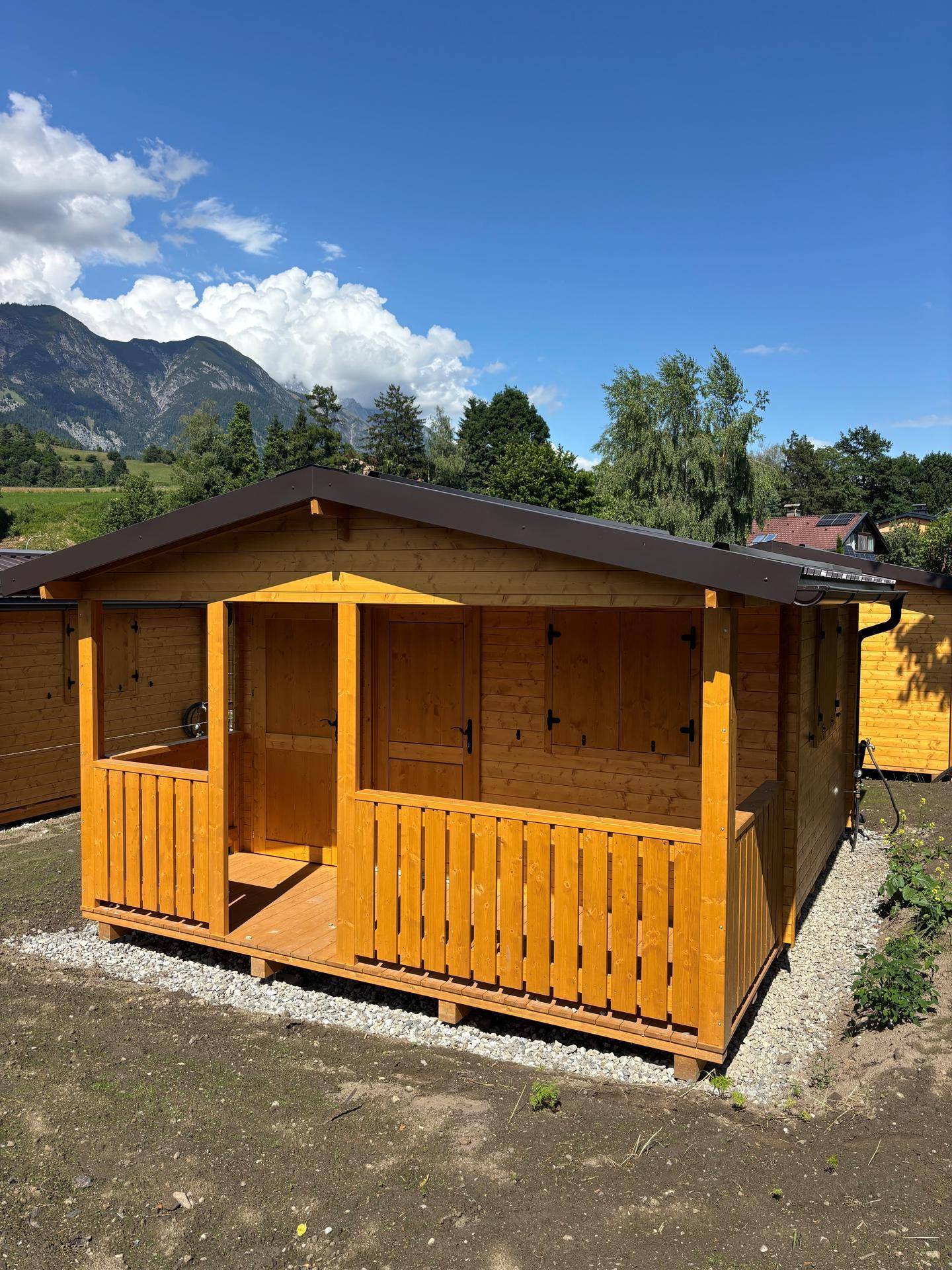 Kleines Holzhaus mit überdachtem Eingangsbereich und Geländer vor einer Berglandschaft.