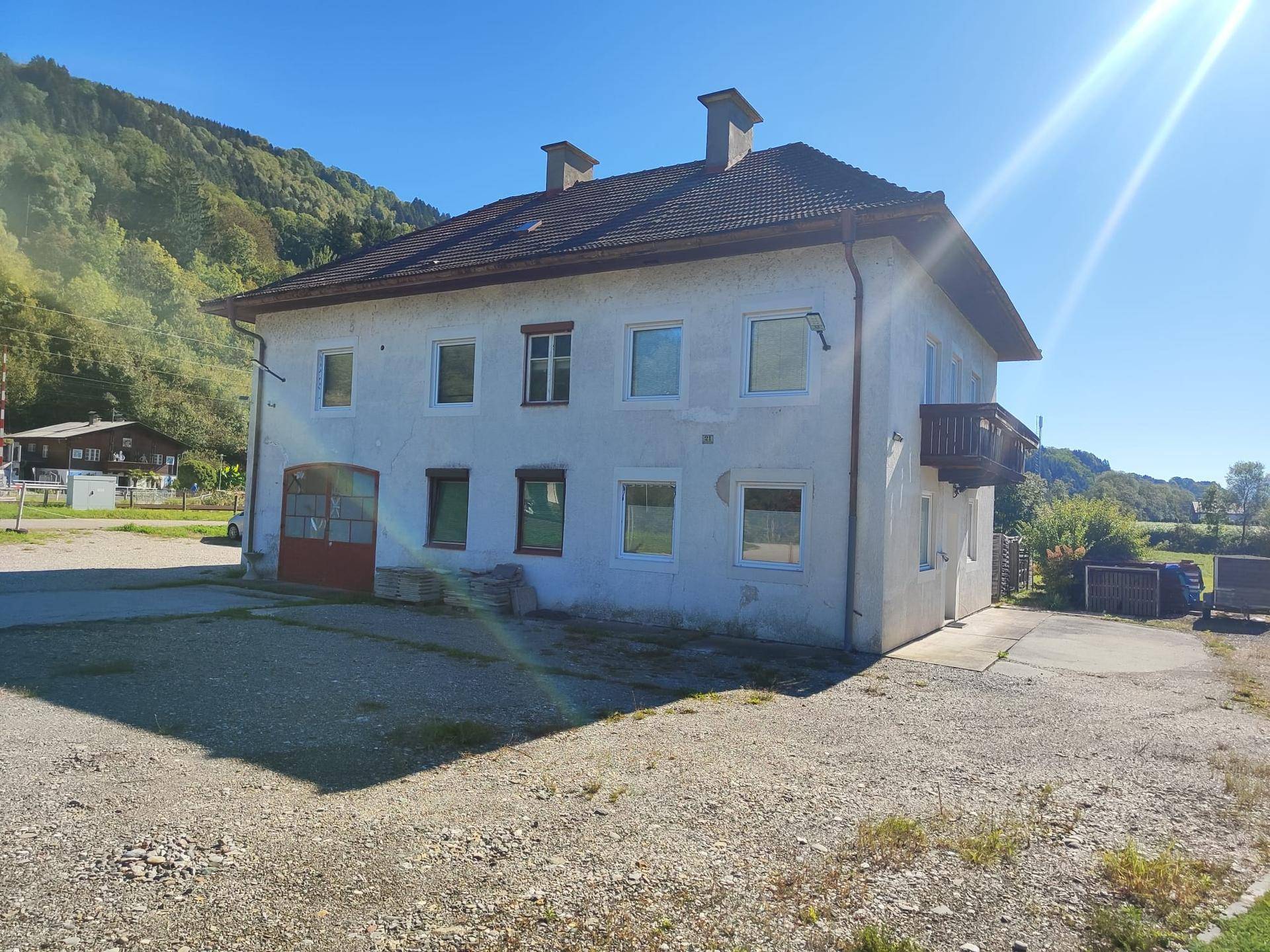 Seitenansicht des Hauses mit mehreren Fenstern und einem Balkon im oberen Stockwerk bei Sonnenschein.