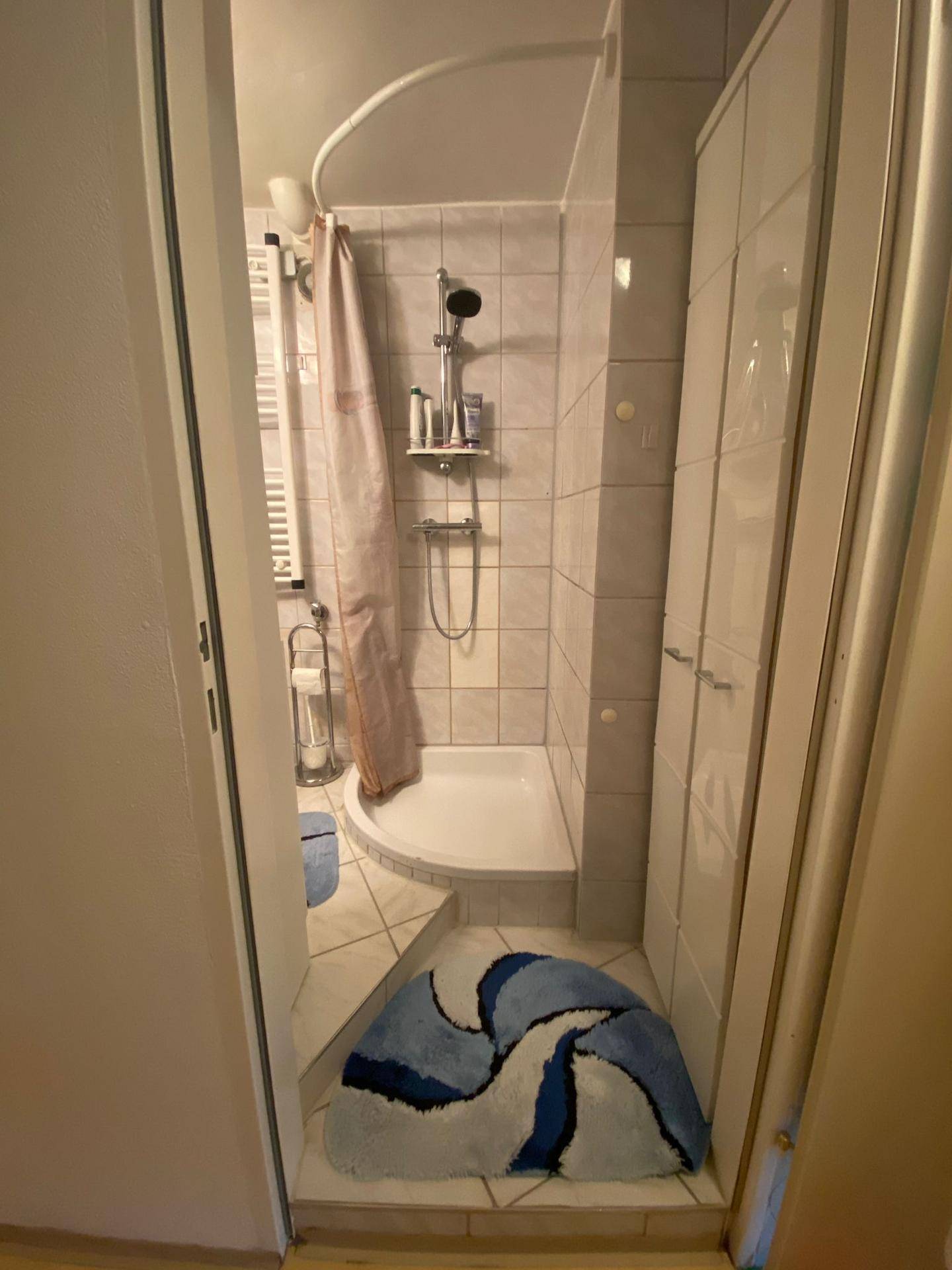 Kleines Badezimmer mit Duschkabine, hellen Fliesen und einem Heizkörper.