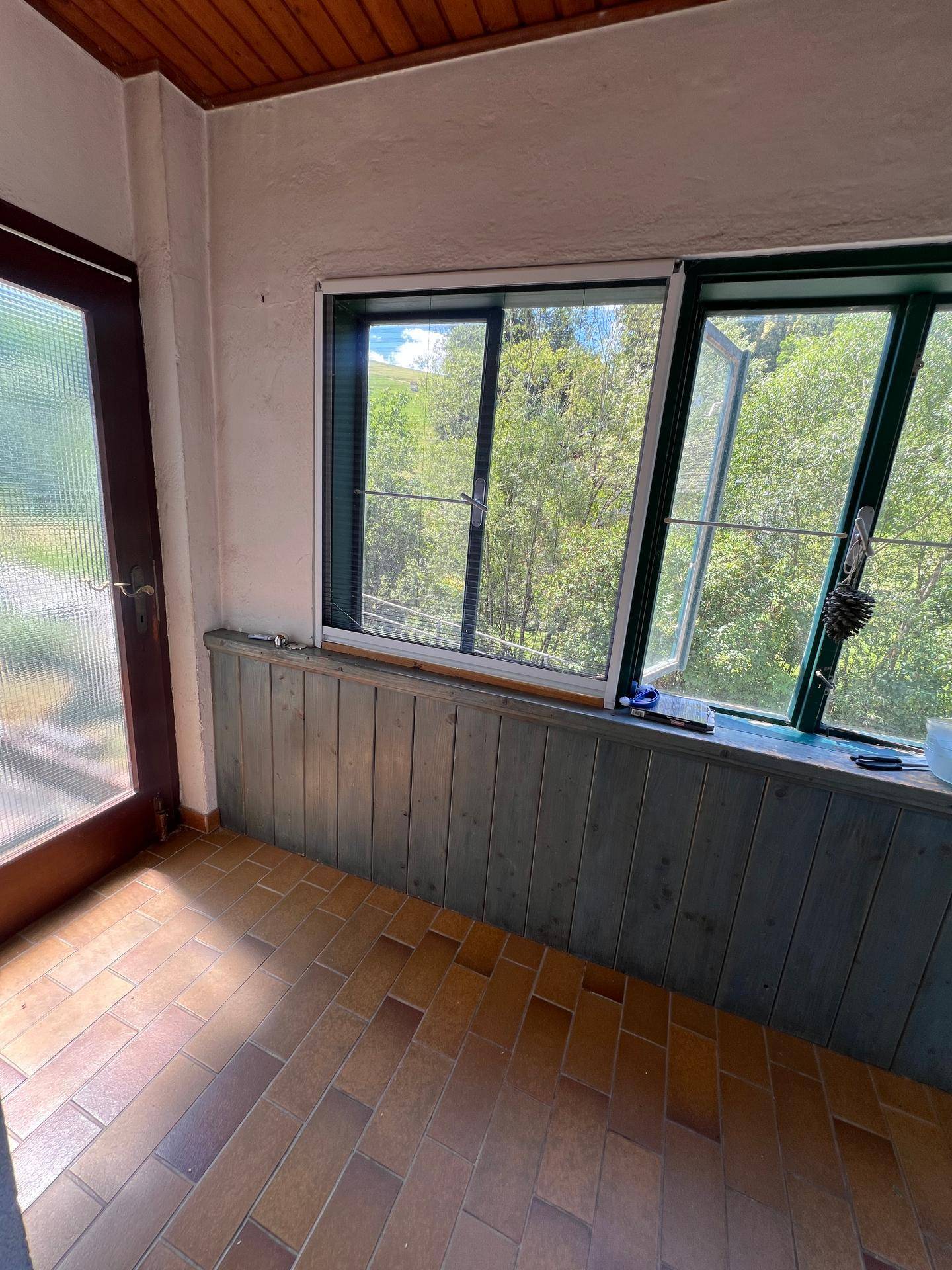 Heller Wintergarten mit großen Fenstern und Blick ins Grüne.