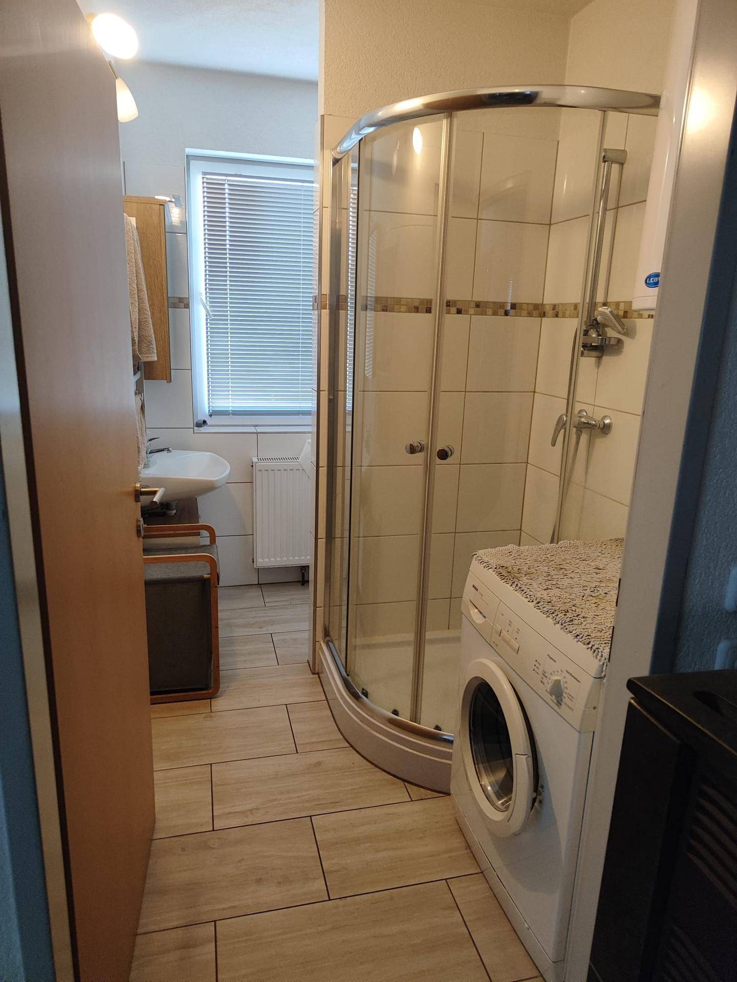 Badezimmer mit Duschkabine, Waschmaschine und Fenster, das viel Licht hereinlässt.