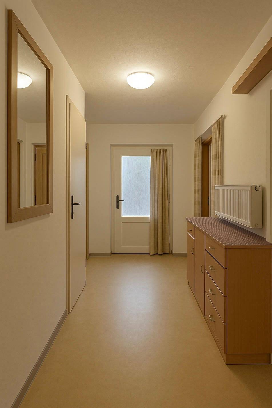 Heller Flur mit Laminatboden, Holzkommode und einem Spiegel an der Wand.