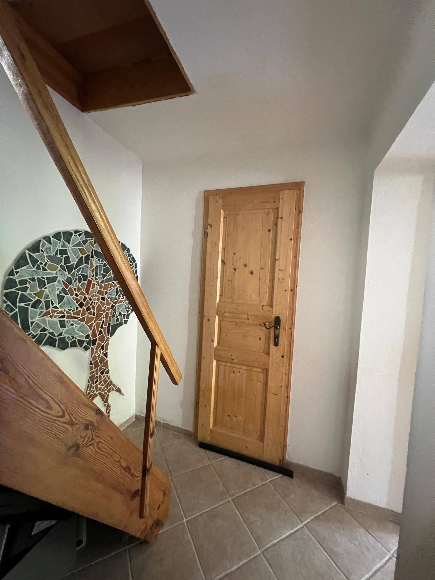 Eingangsbereich mit Holztreppe, Fliesenboden und einer Holztür.