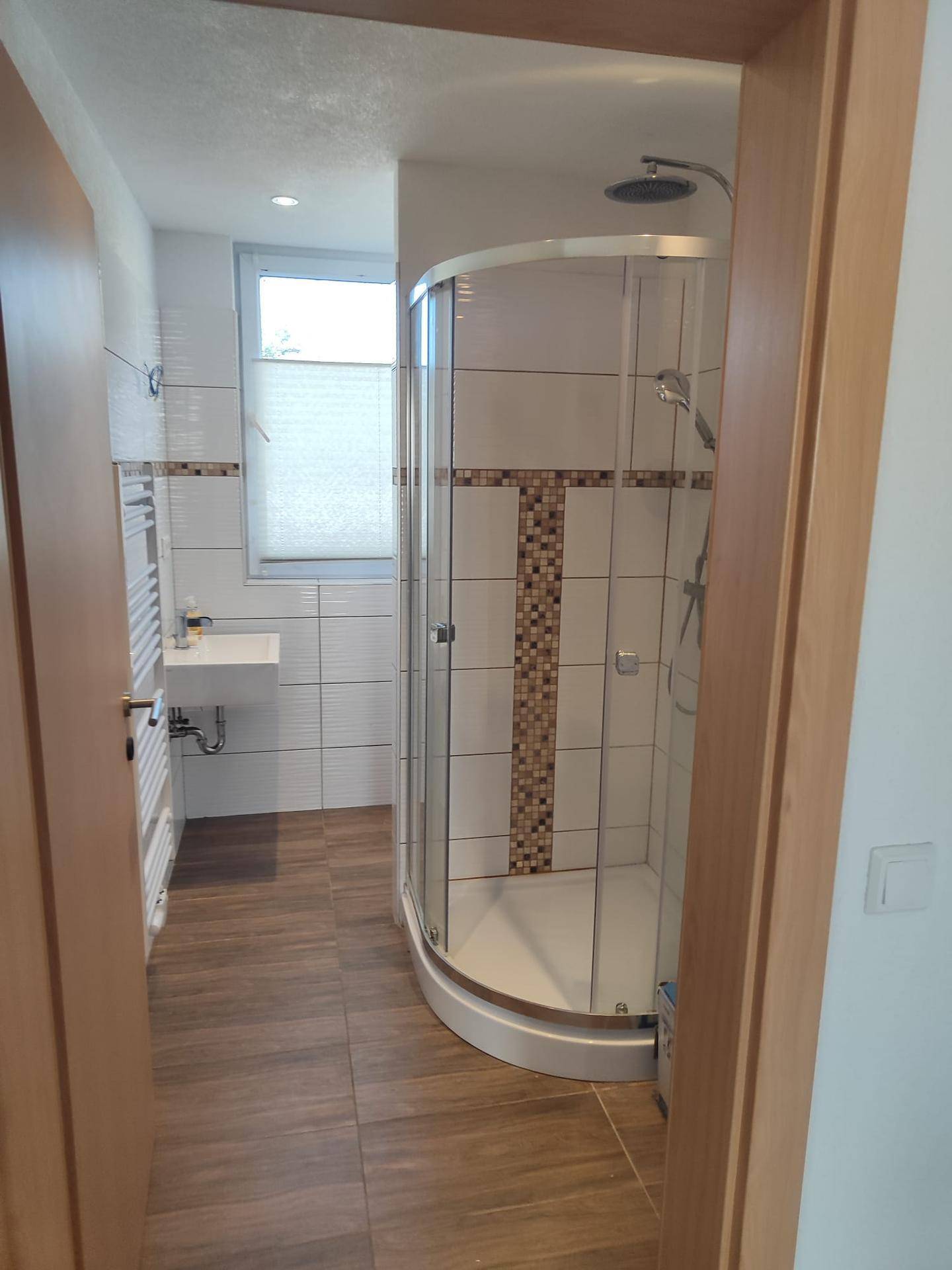 Modernes Badezimmer mit Duschkabine, kleinem Waschbecken und Fenster für natürliches Tageslicht.