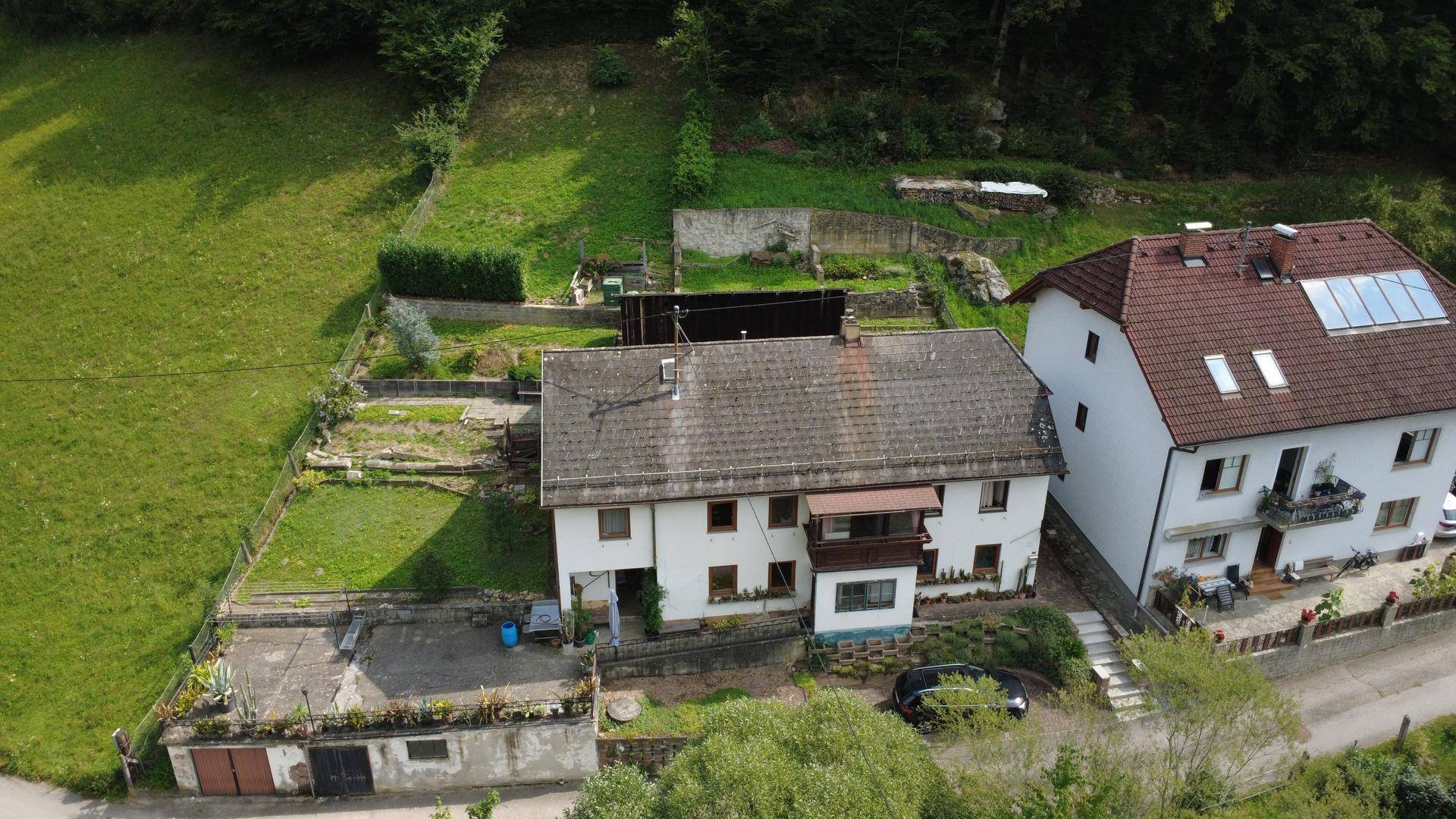 Luftaufnahme von zwei Wohnhäusern mit Gärten und umliegender grüner Landschaft.