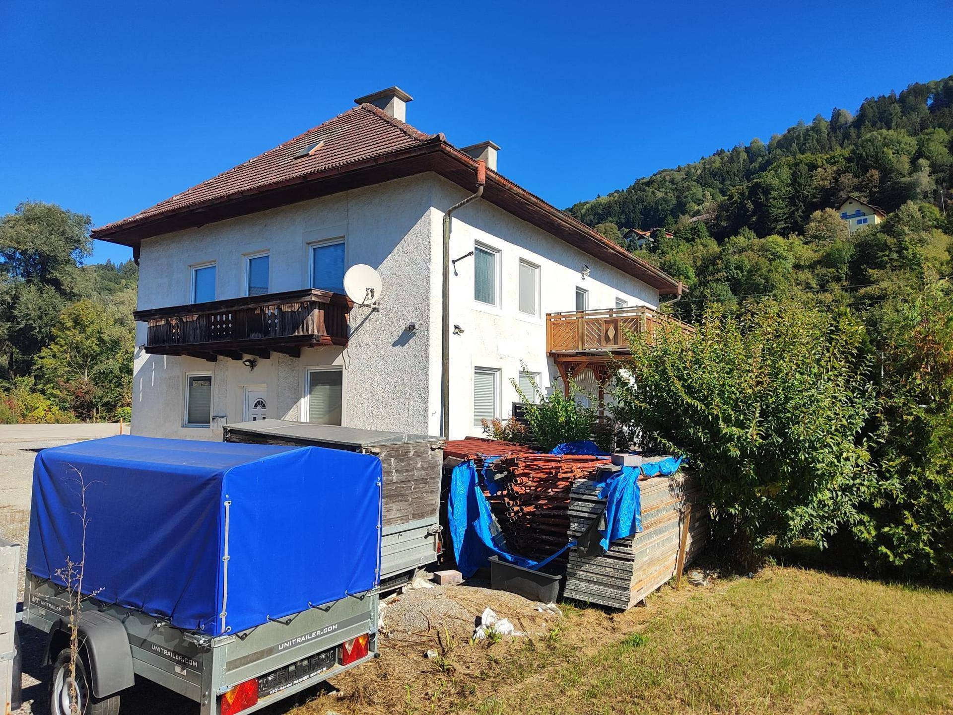 Rückansicht des Hauses mit zwei Balkonen und Blick auf die bewaldeten Hügel unter klarem Himmel.