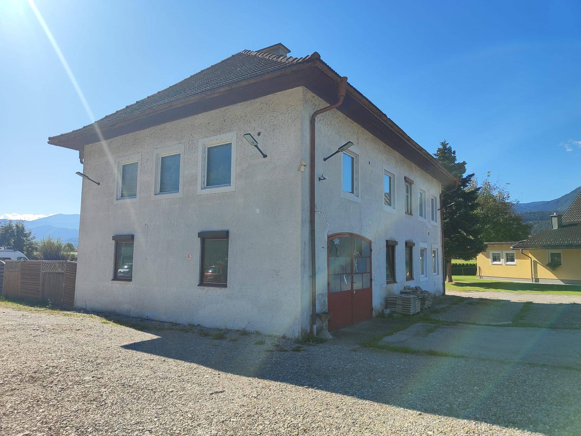 Seitenansicht des Hauses mit mehreren Fenstern und einem roten Garagentor unter strahlendem Sonnenschein.