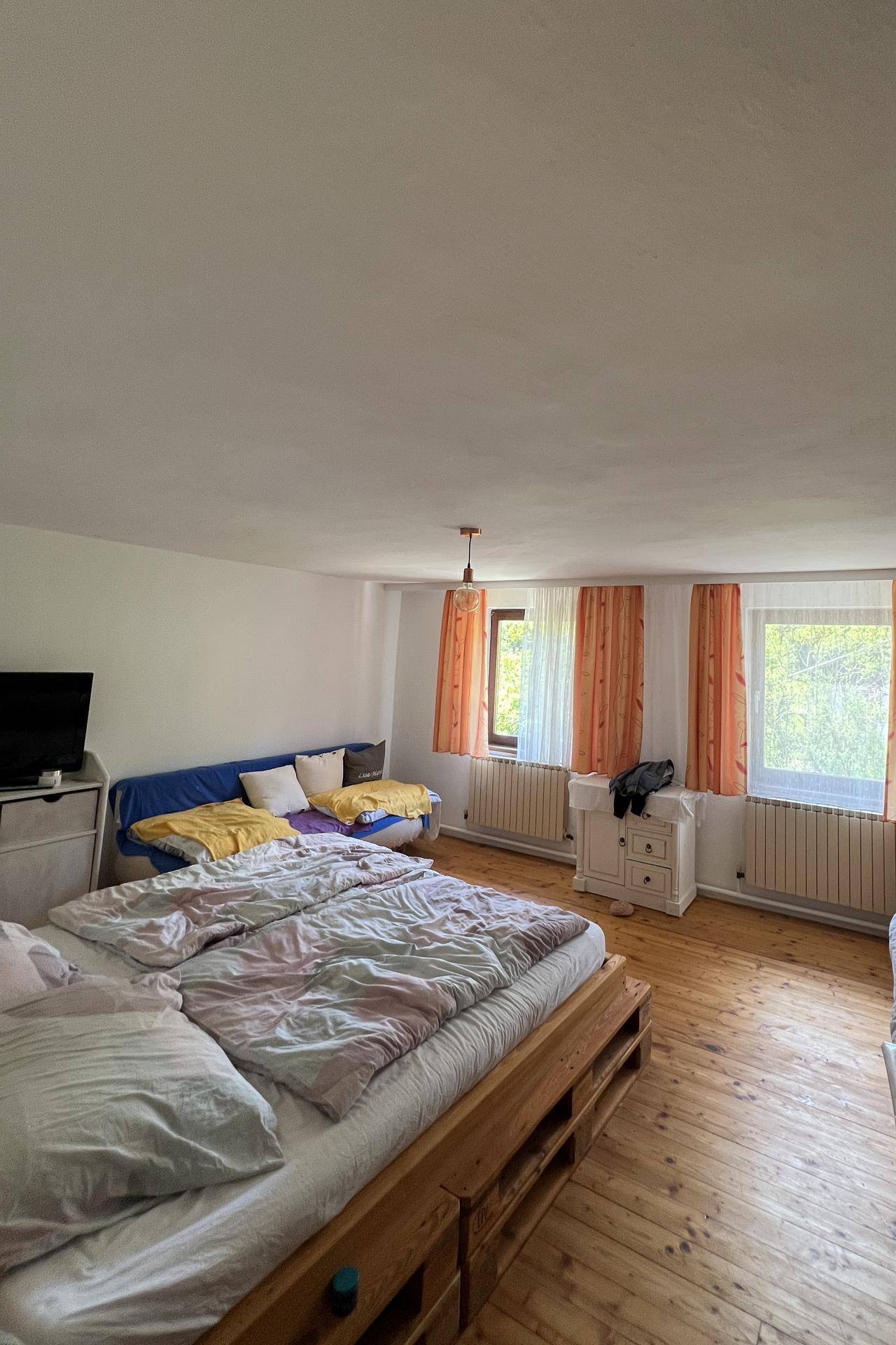 Geräumiges Schlafzimmer mit Holzboden, Doppelbett und mehreren Fenstern.