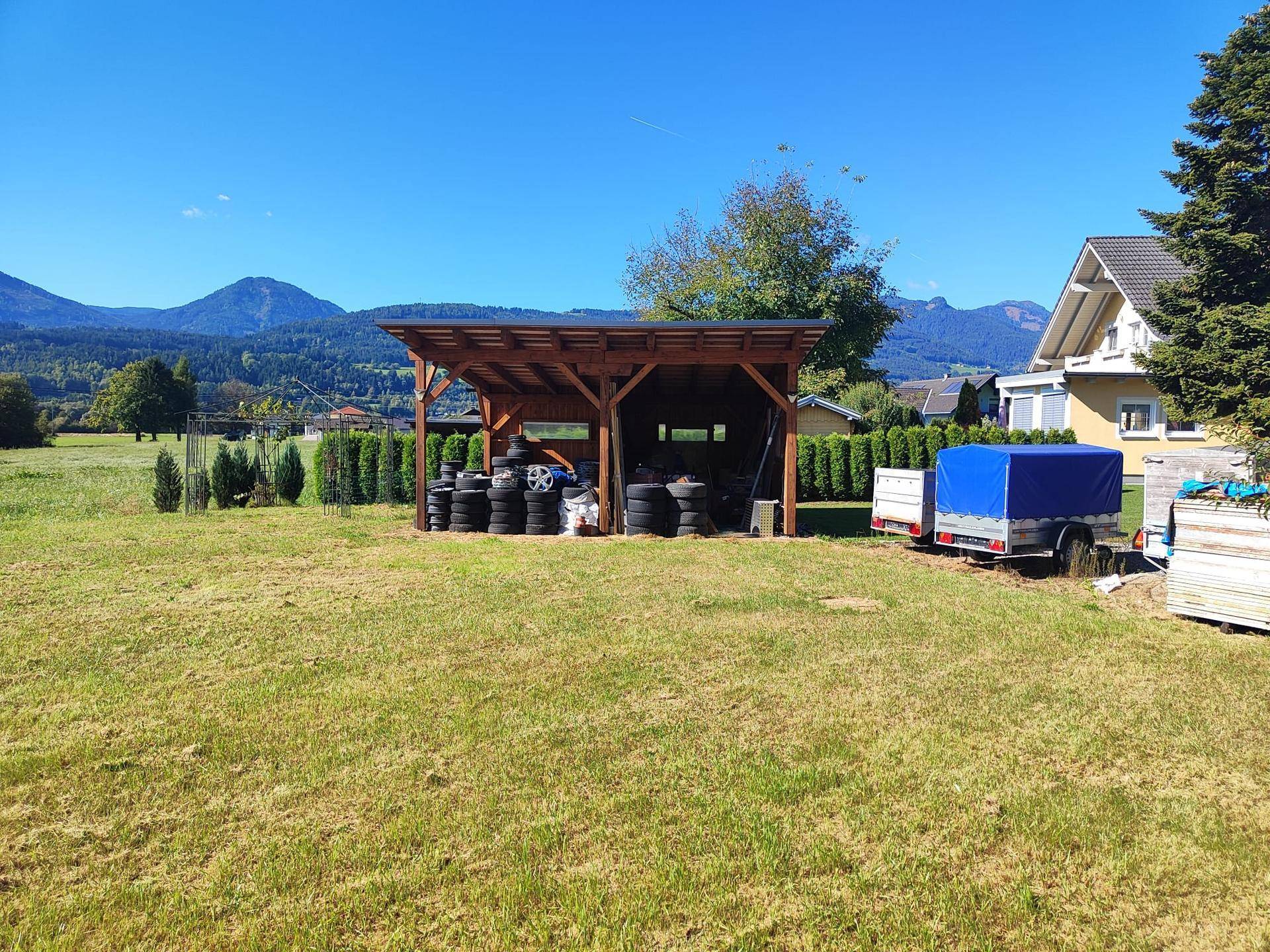 Offener Unterstand im Grünen mit gelagerten Reifen und Blick auf die Berge unter blauem Himmel.