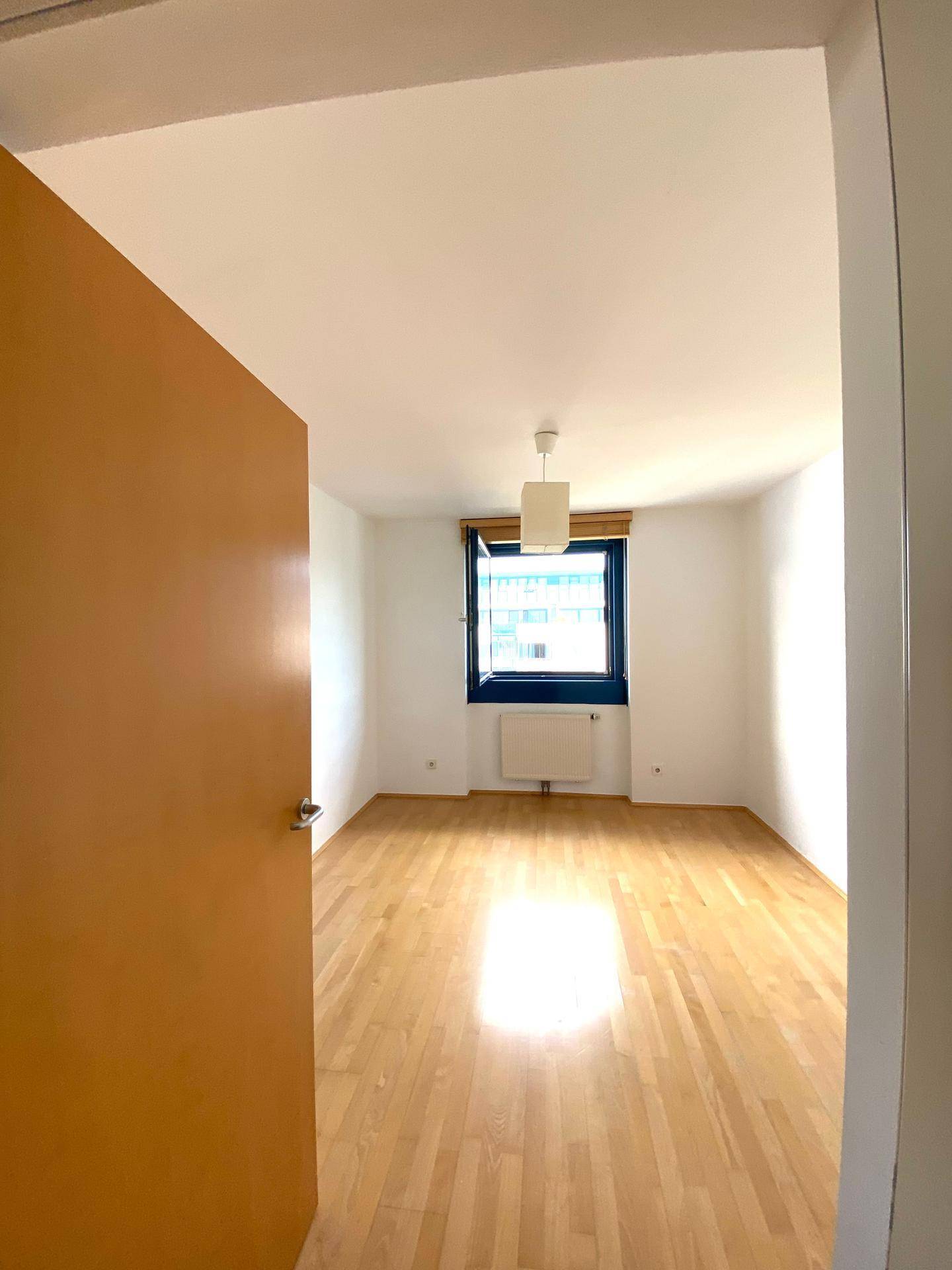 Helles Schlafzimmer mit Holzboden und einem Fenster, das eine angenehme Atmosphäre schafft.