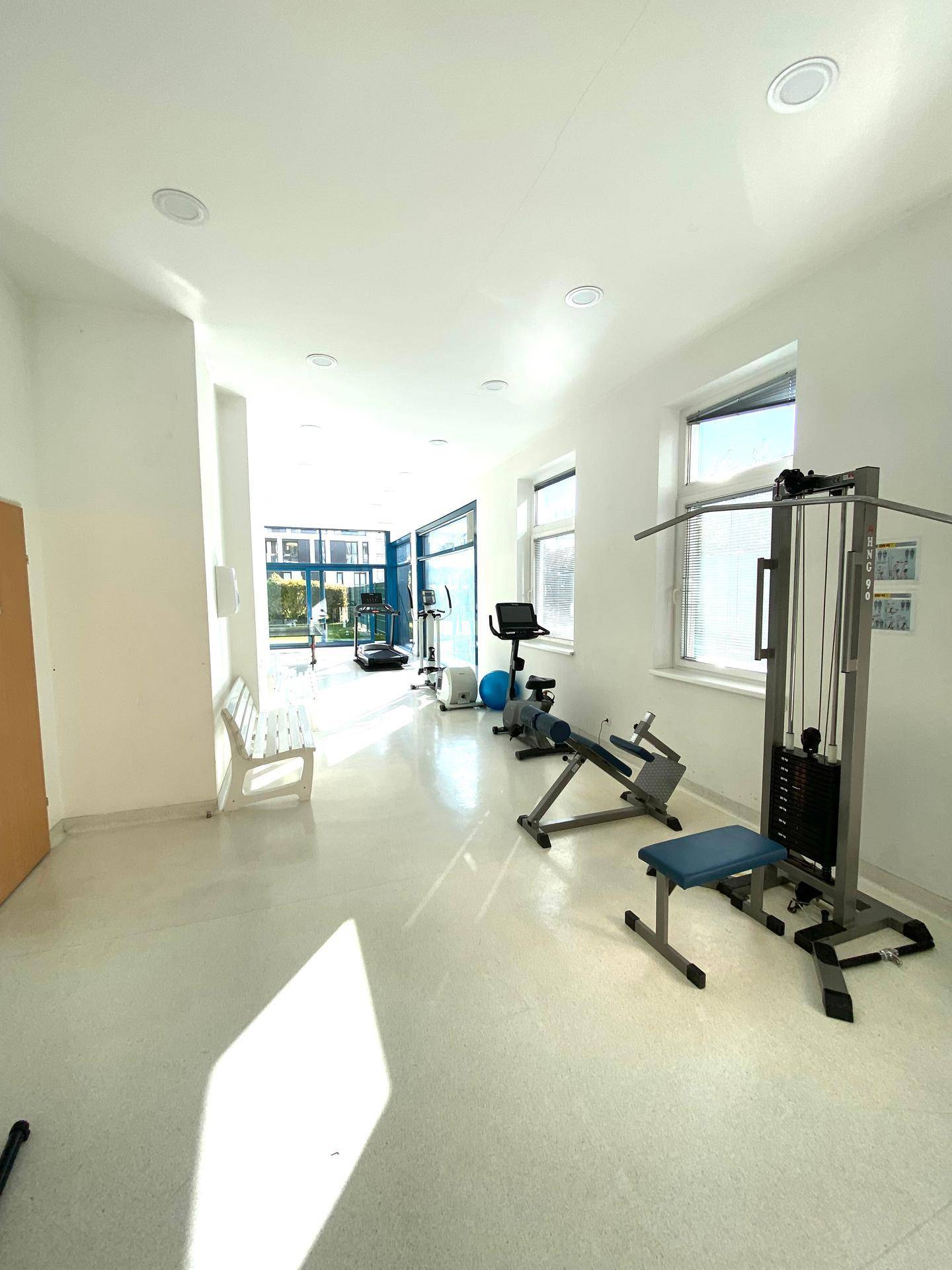 Gut ausgestatteter Fitnessraum mit verschiedenen Trainingsgeräten und viel Tageslicht.