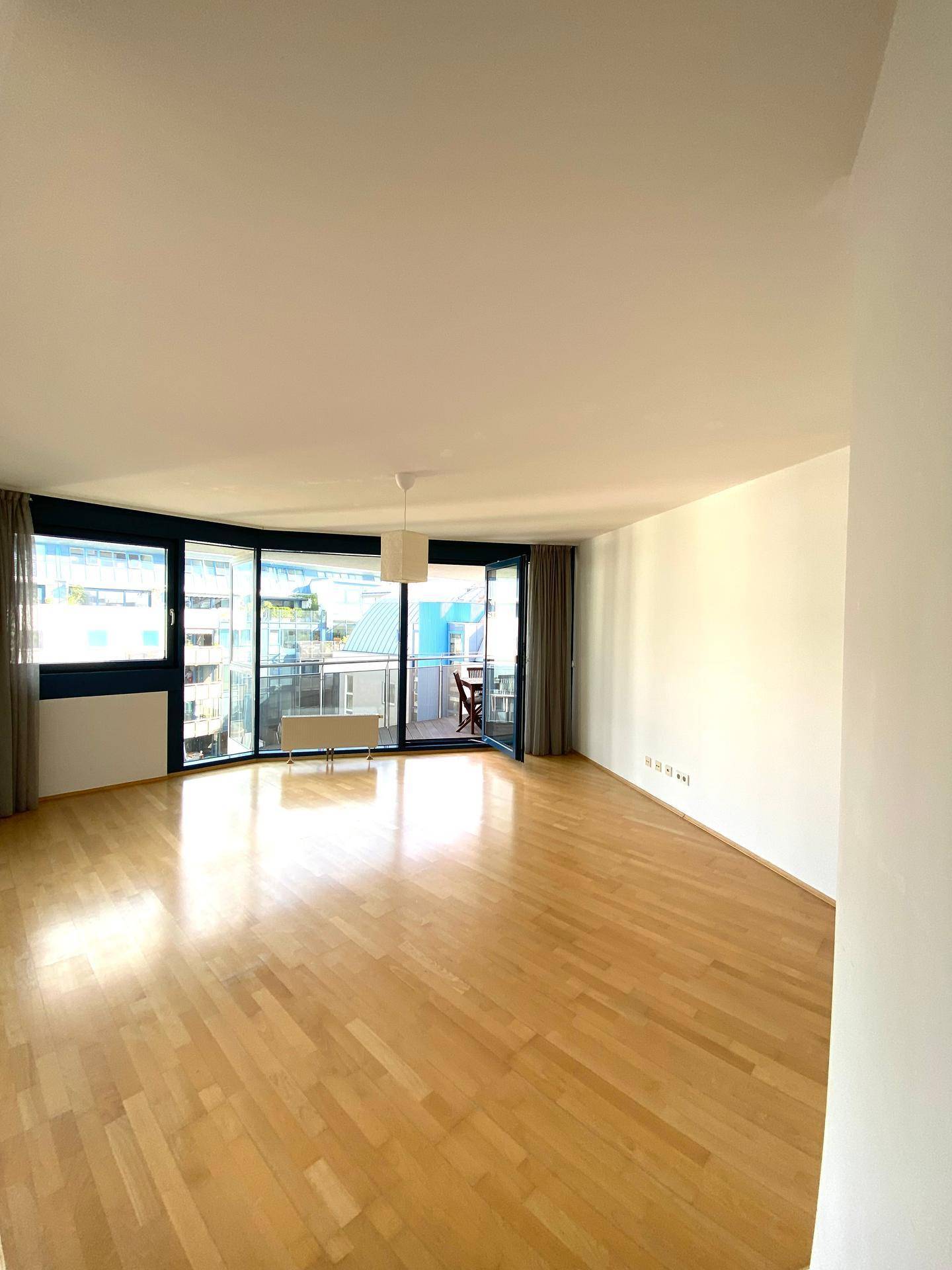 Helles Wohnzimmer mit Holzboden und großen Fenstern, die Zugang zu einem Balkon bieten.