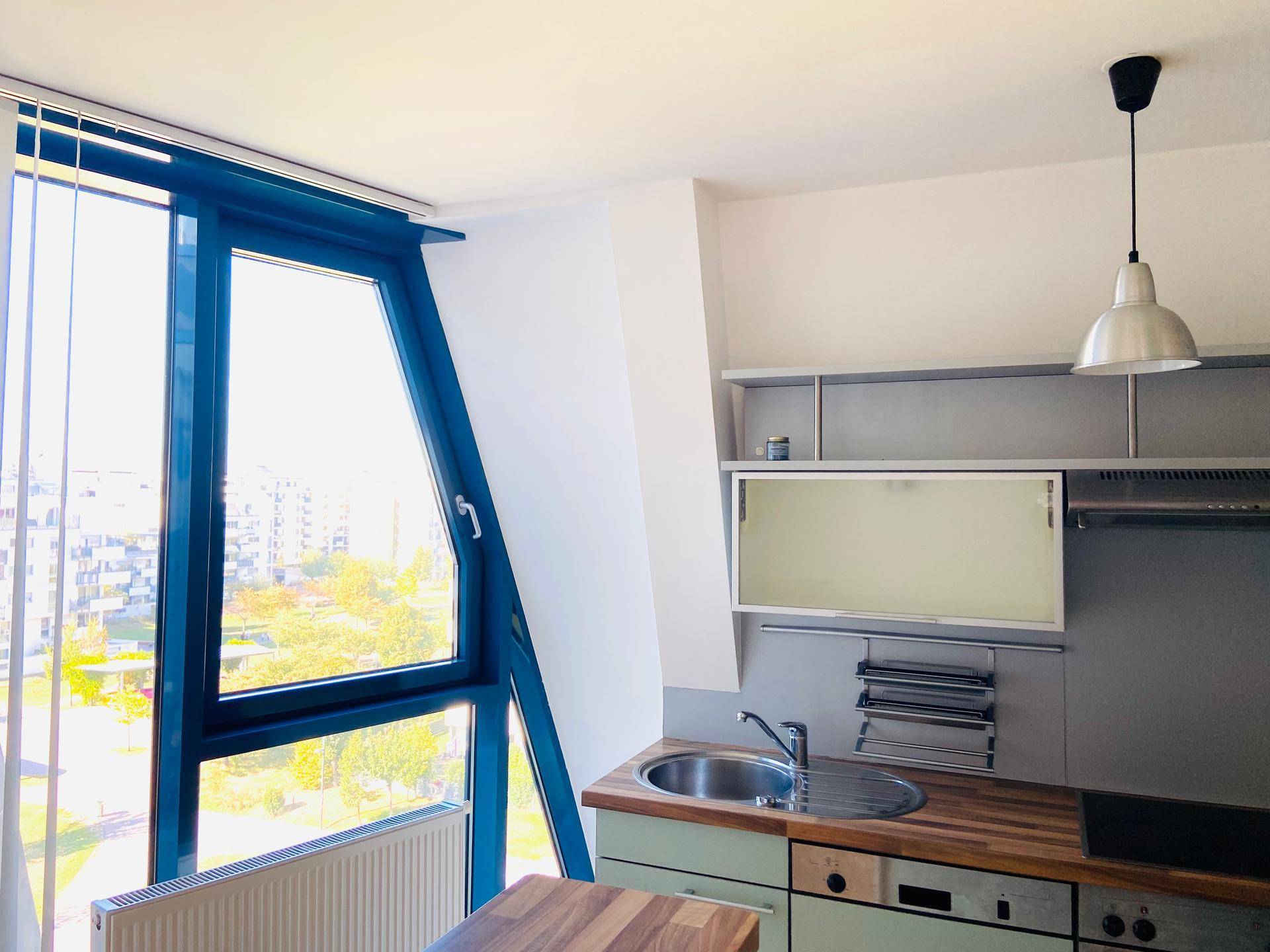 Helle Küchenzeile mit Holzarbeitsplatte und einem großen, schrägen Fenster mit Stadtblick.