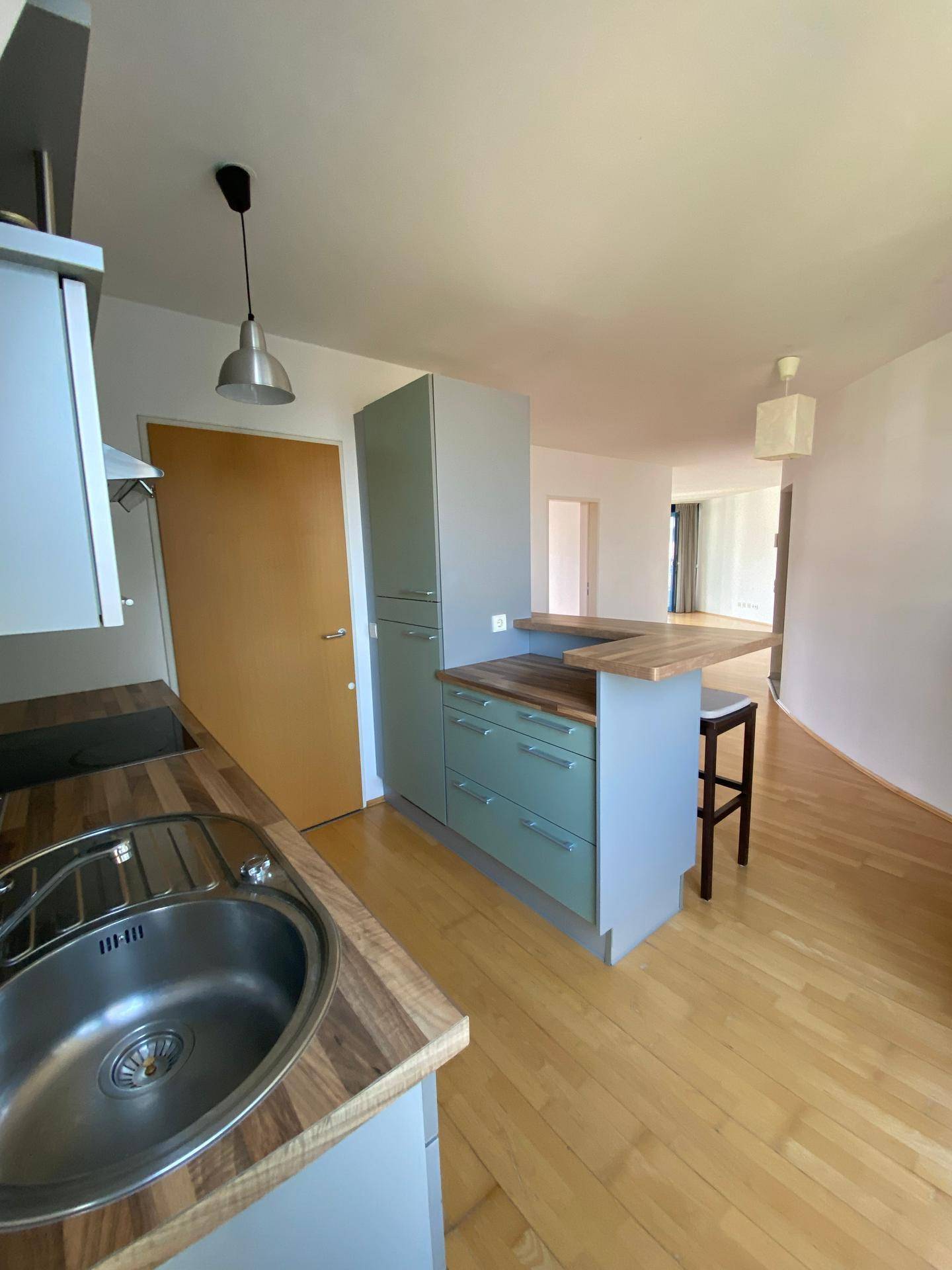 Moderne Küche mit Frühstücksbar und Holzboden, offen zum angrenzenden Wohnbereich.