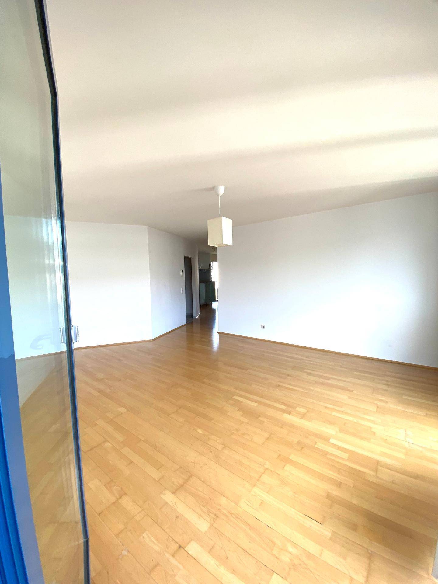 Geräumiges, leeres Wohnzimmer mit hellem Holzboden und weißen Wänden, bereit zur Einrichtung.
