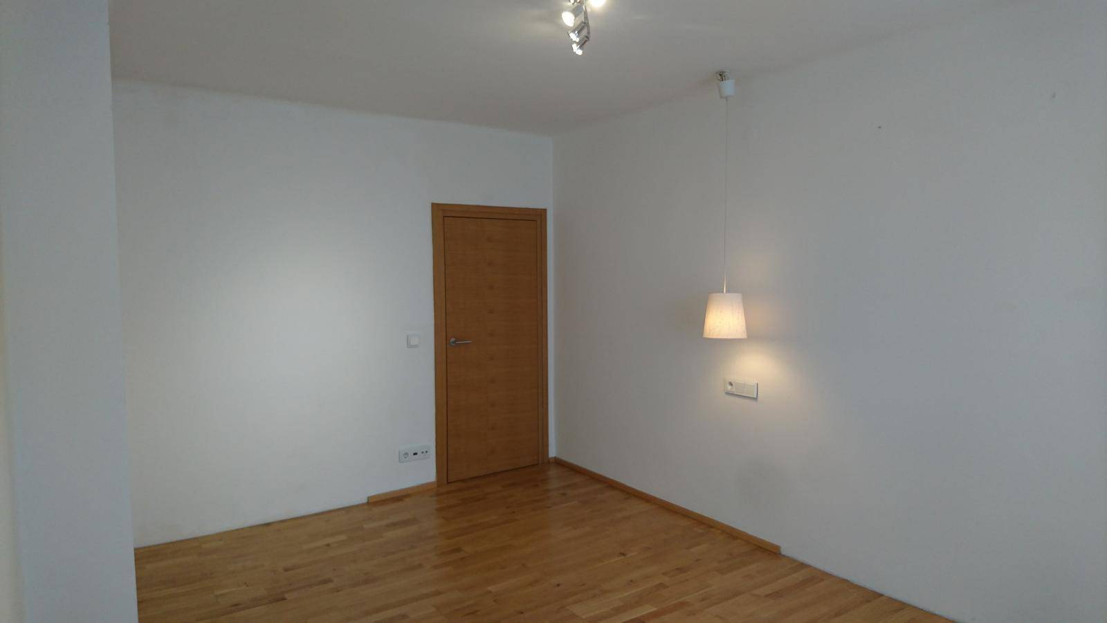 Helles Zimmer mit Parkettboden und Holztür, ausgestattet mit einer Pendelleuchte.