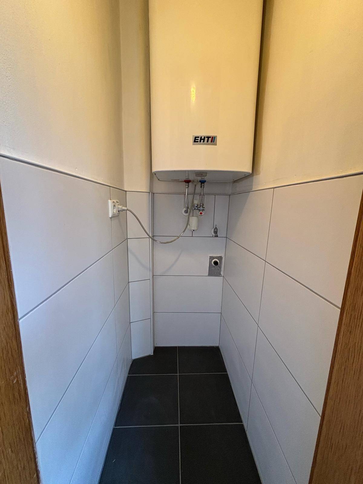 Kleiner Hauswirtschaftsraum mit Warmwasserboiler und Fliesenboden.