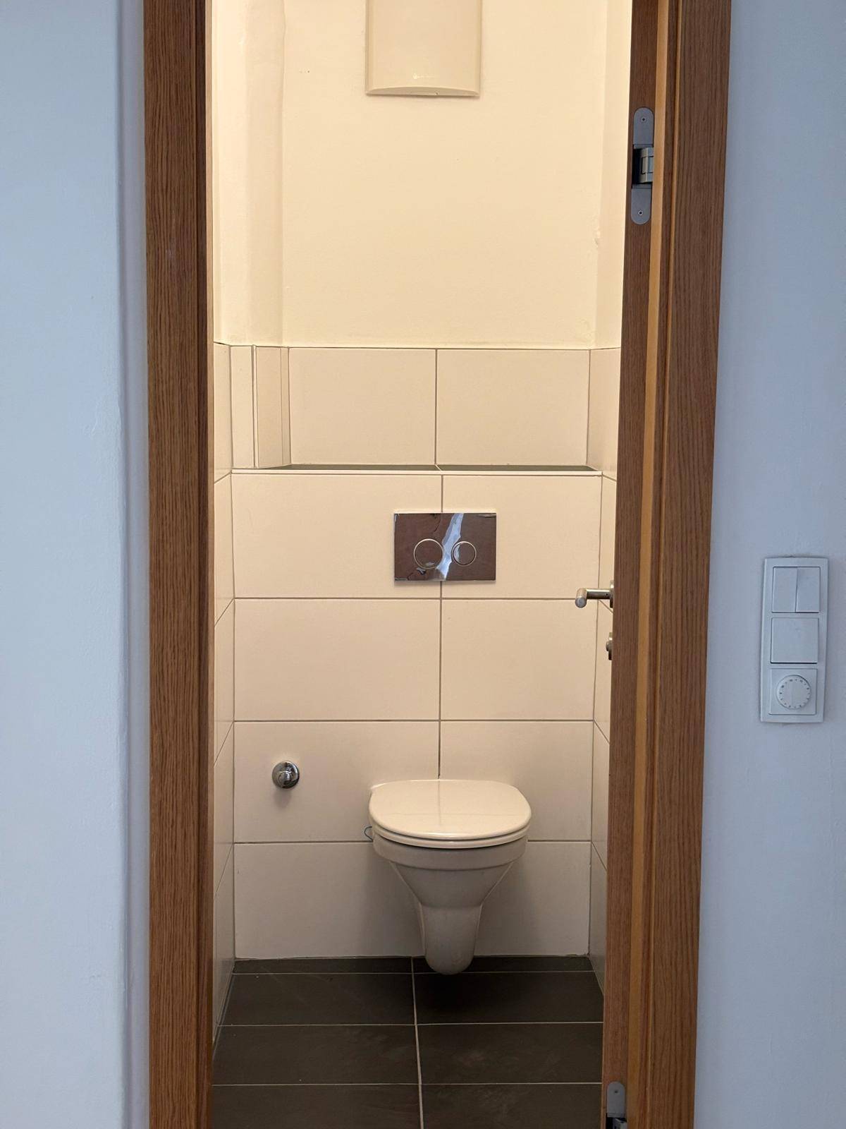 Modern gefliestes Gäste-WC mit wandhängender Toilette und dunklem Boden.