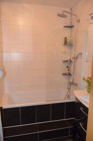 Badezimmer mit Badewanne, Duscharmatur und weißen Wandfliesen.